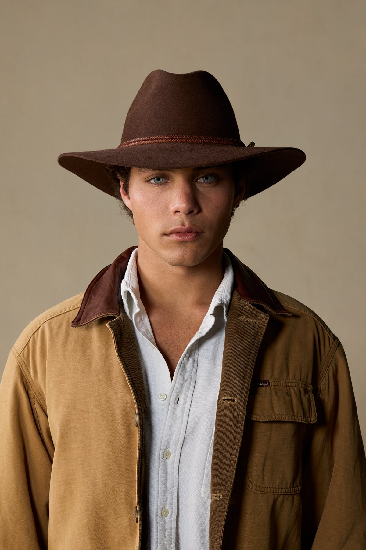 Brown fur felt cowboy hat with leather trim on model wearing tan jacket and white shirt