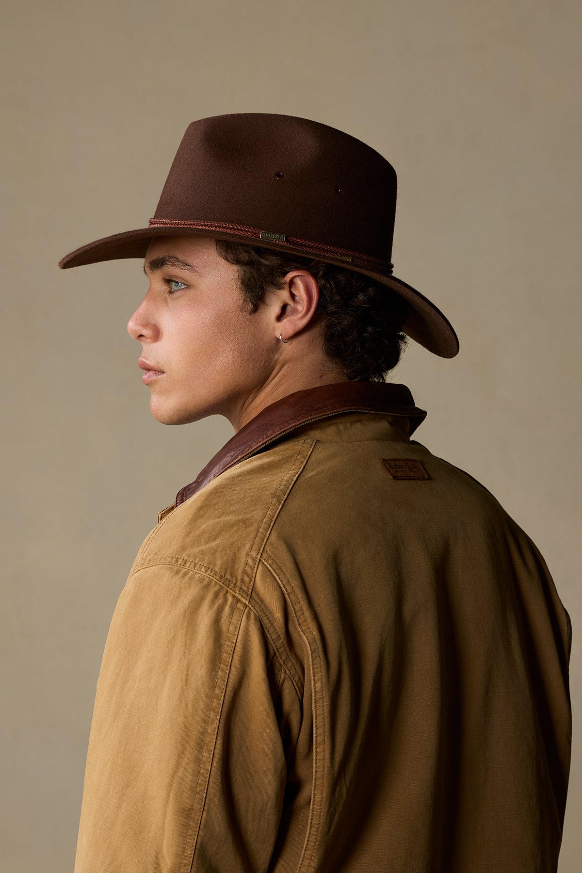 Brown rabbit fur traveller hat with braided band, worn by person in tan jacket, side profile view