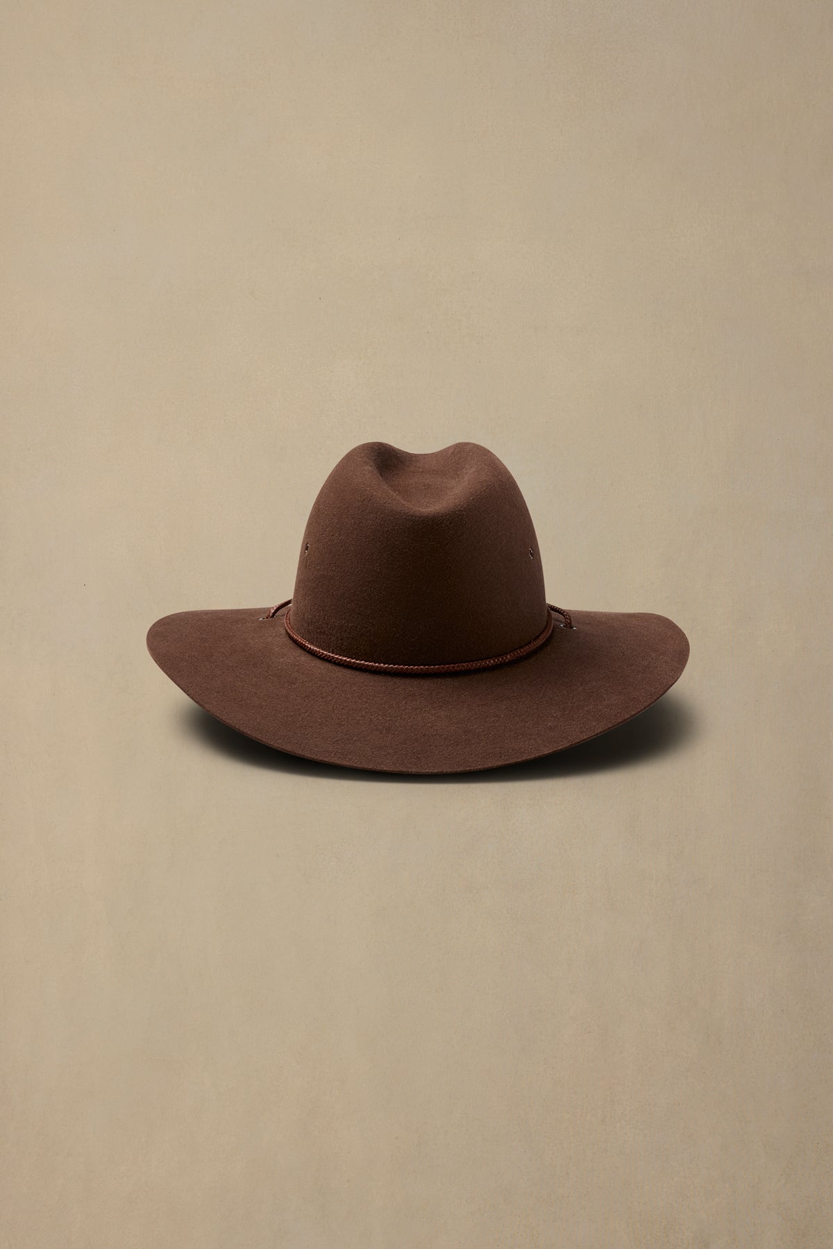 Brown rabbit fur traveller hat with rope trim against neutral background