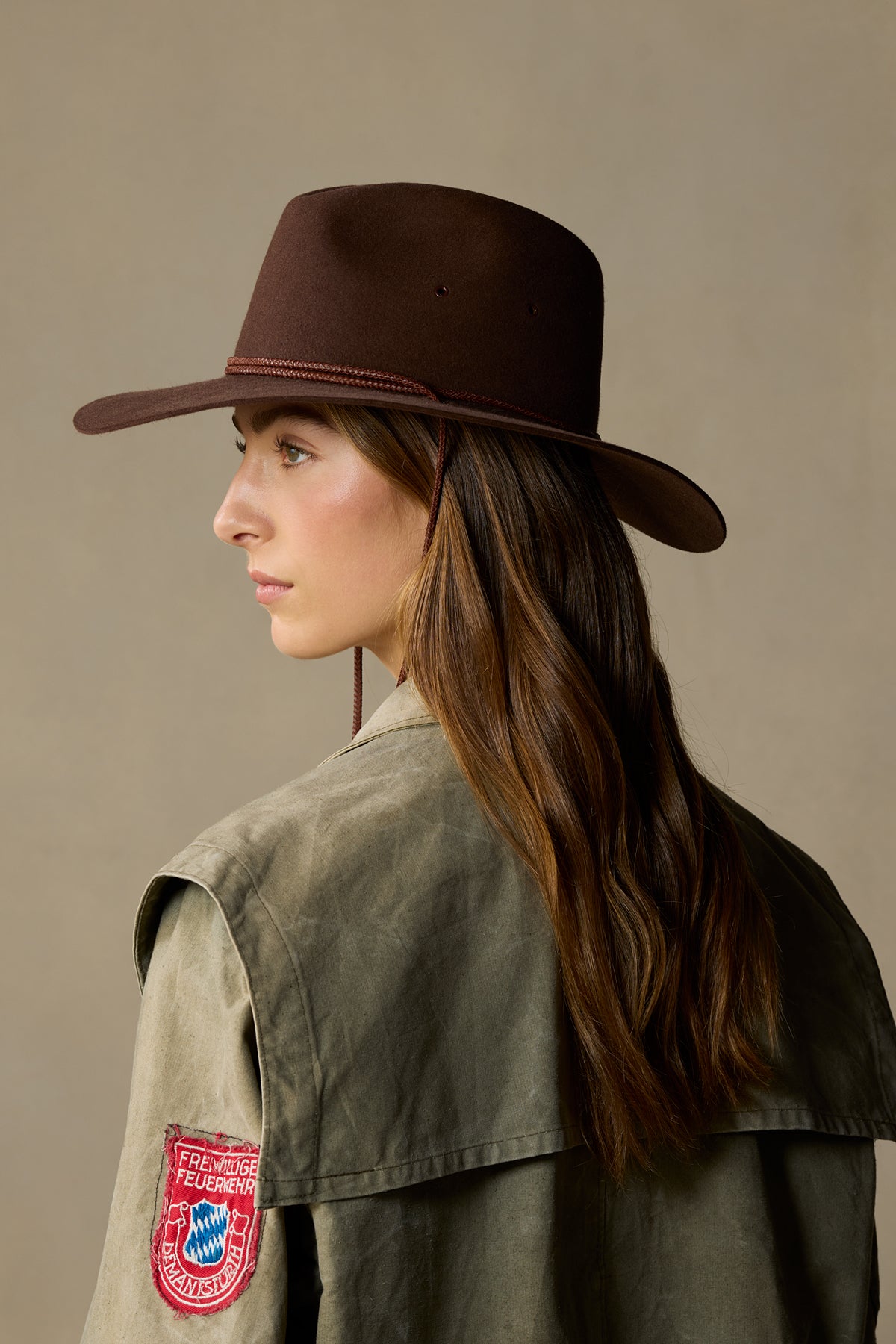 Brown fur felt traveller hat with cord detail on woman wearing vintage-style jacket, side profile view