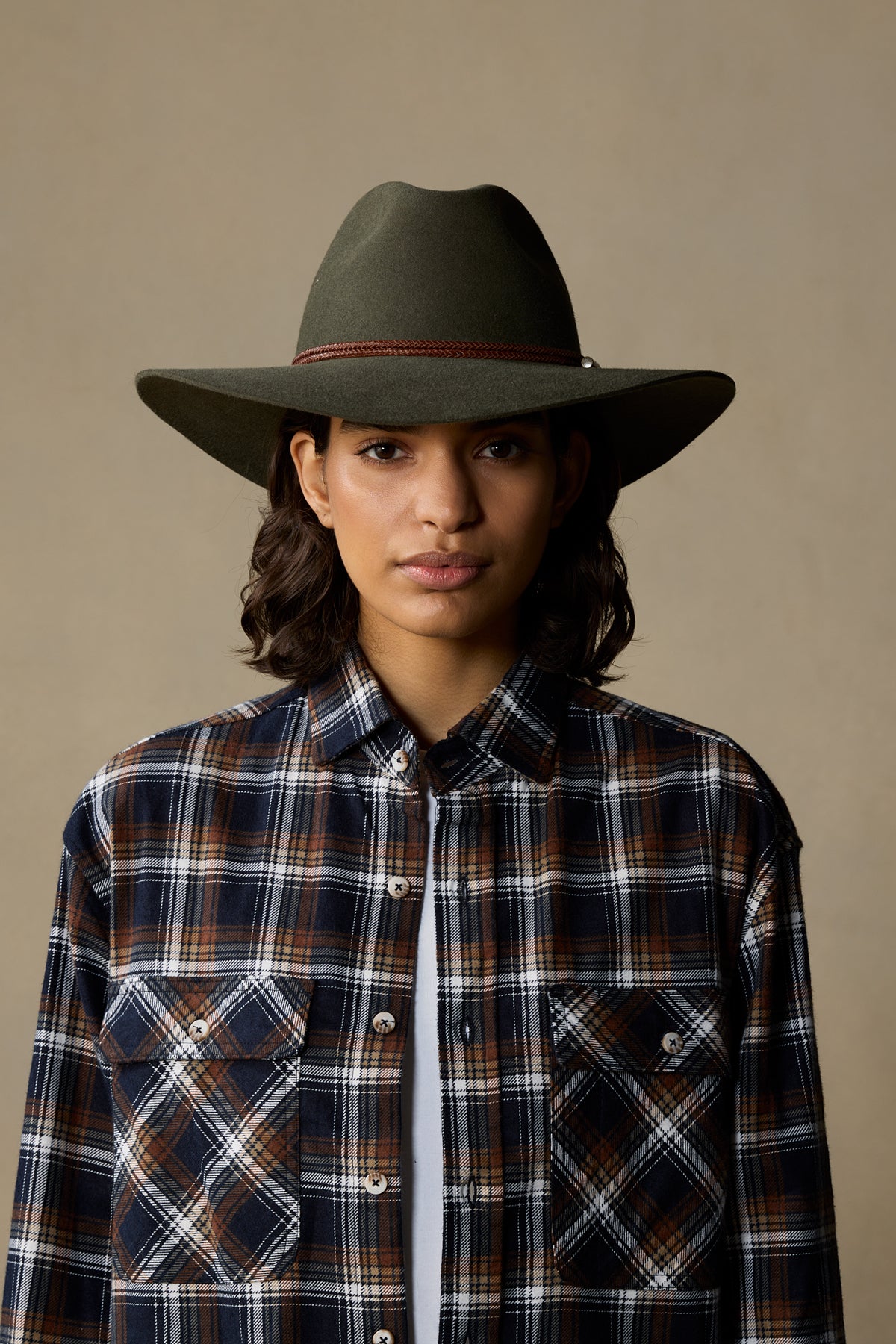Person wearing fern-colored rabbit fur cowboy hat with plaid shirt against neutral background