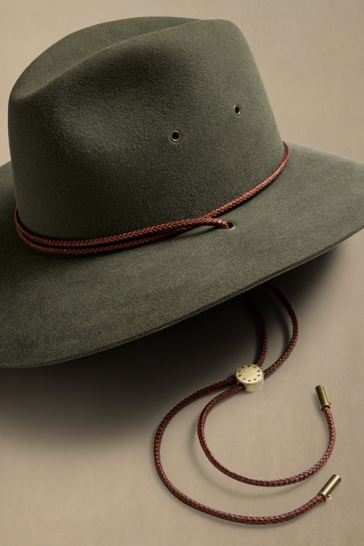 Sage green rabbit fur Traveller hat with burgundy braided cord and decorative slide detail against neutral background