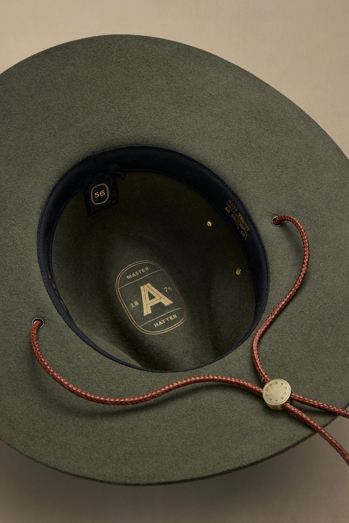 Fern green rabbit fur traveller hat displayed flat lay showing interior label and burgundy chin cord with brass toggle