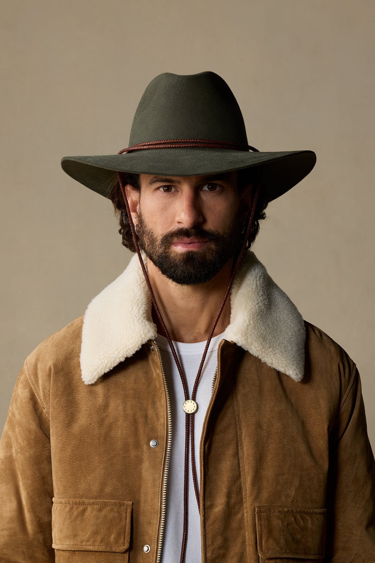 Charcoal wool cowboy hat with braided chin strap on bearded man in tan suede jacket with sherpa collar