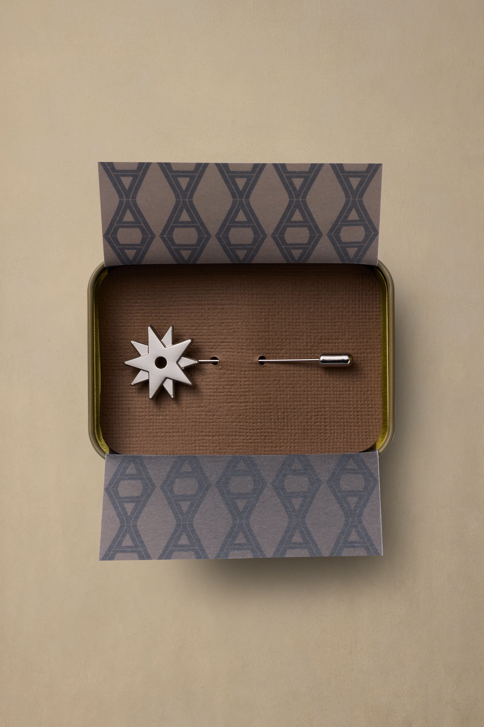 Spur pewter star pin displayed in branded box with brown textured interior and geometric patterned lid