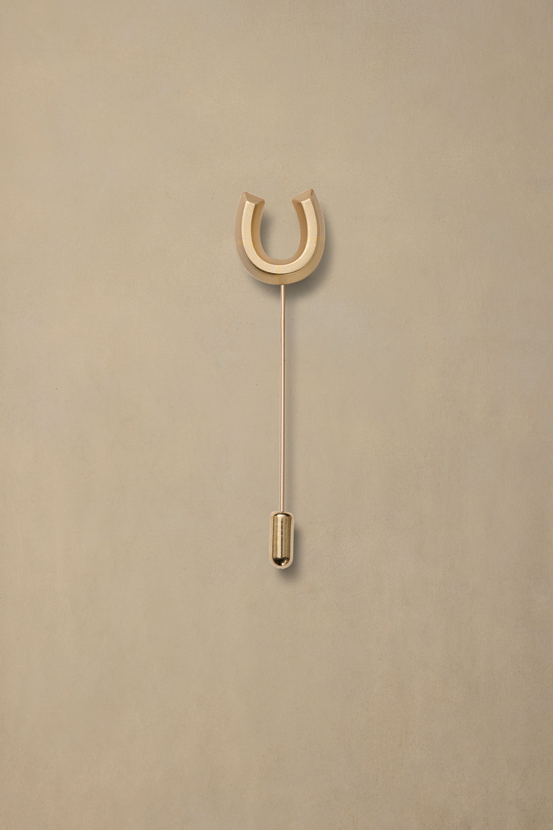 Gold horseshoe pin with long stem on neutral beige background