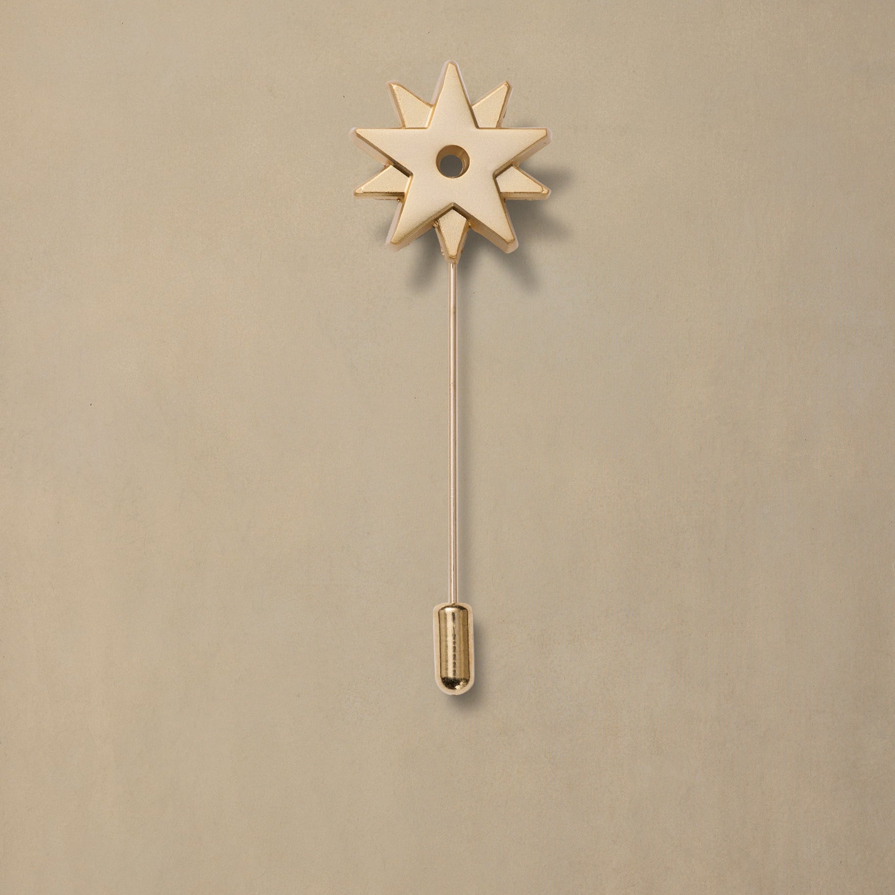 Brass spur pin with eight-pointed star head and long stem on beige background