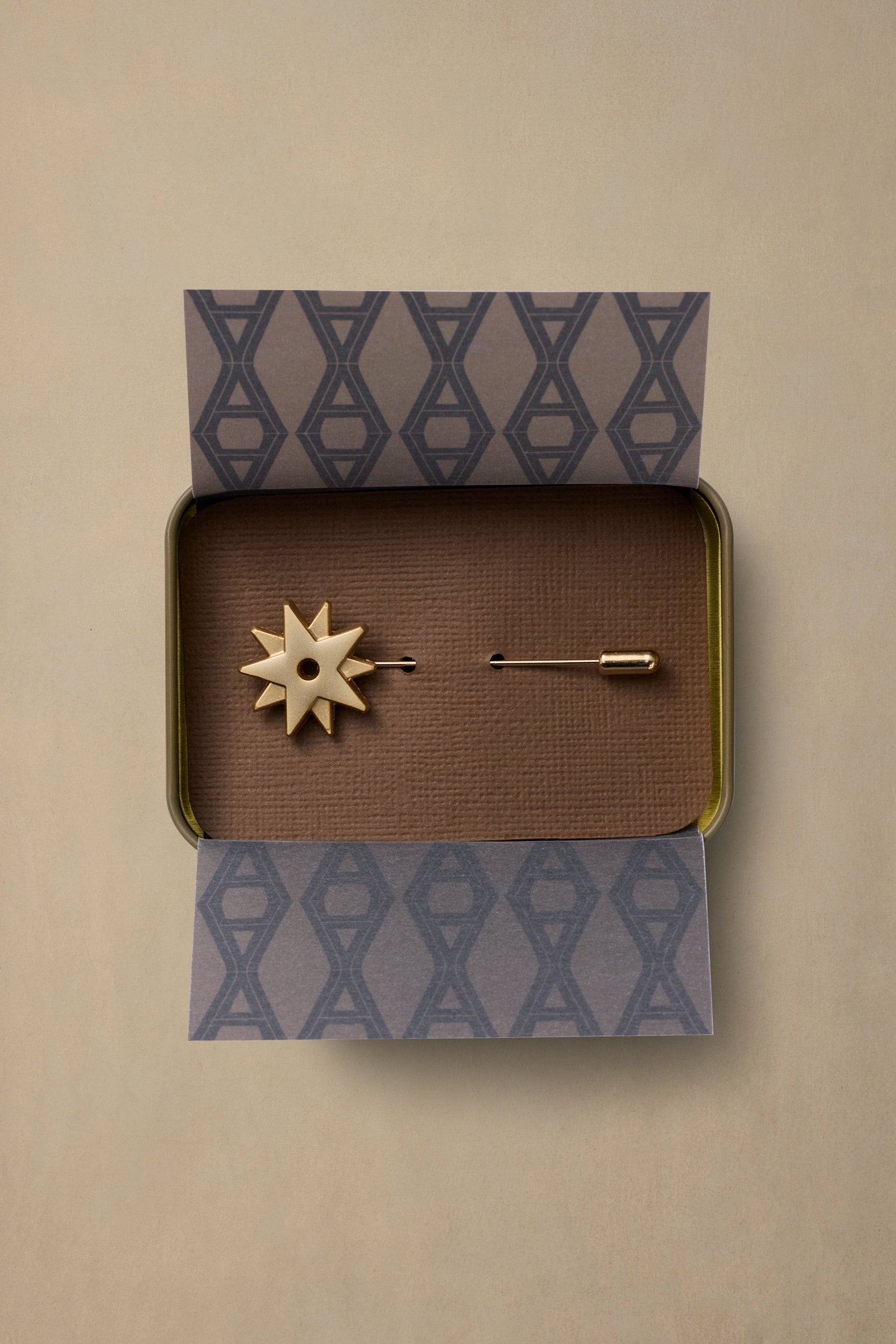 Brass spur pin with eight-pointed star design displayed in patterned gift box with brown textured interior on cream background