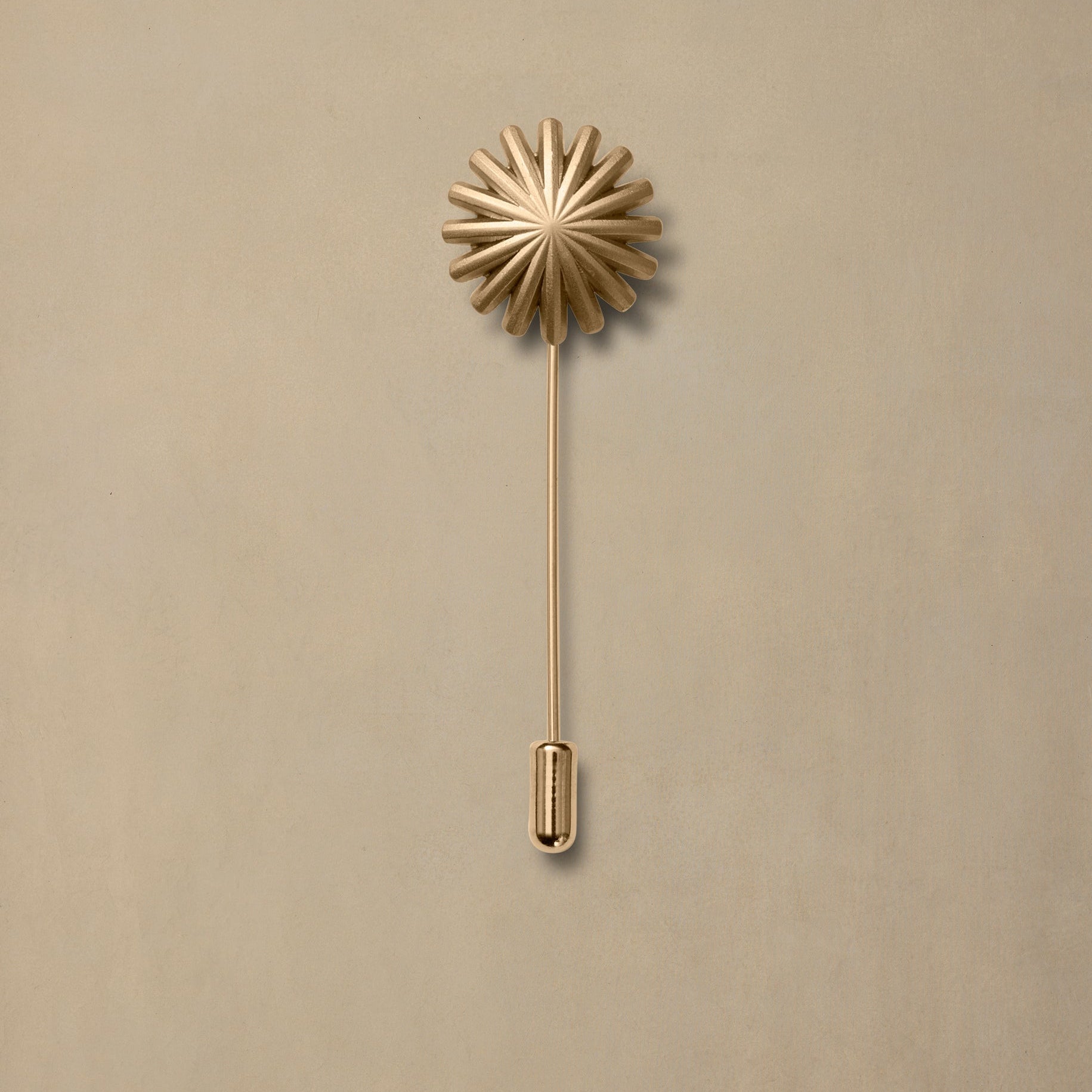 Gold daisy flower lapel pin with long stem on neutral beige background