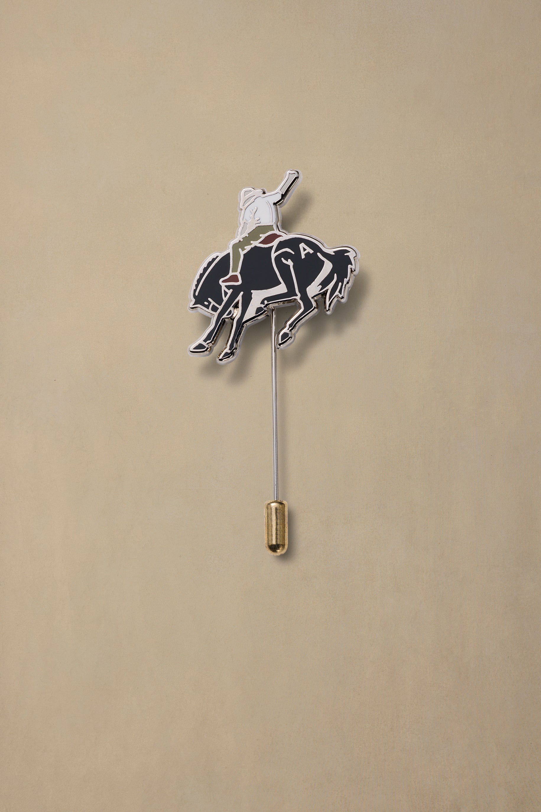 Bucking Bronc enamel pin with cowboy rider on black horse, gold clutch backing, displayed against tan background