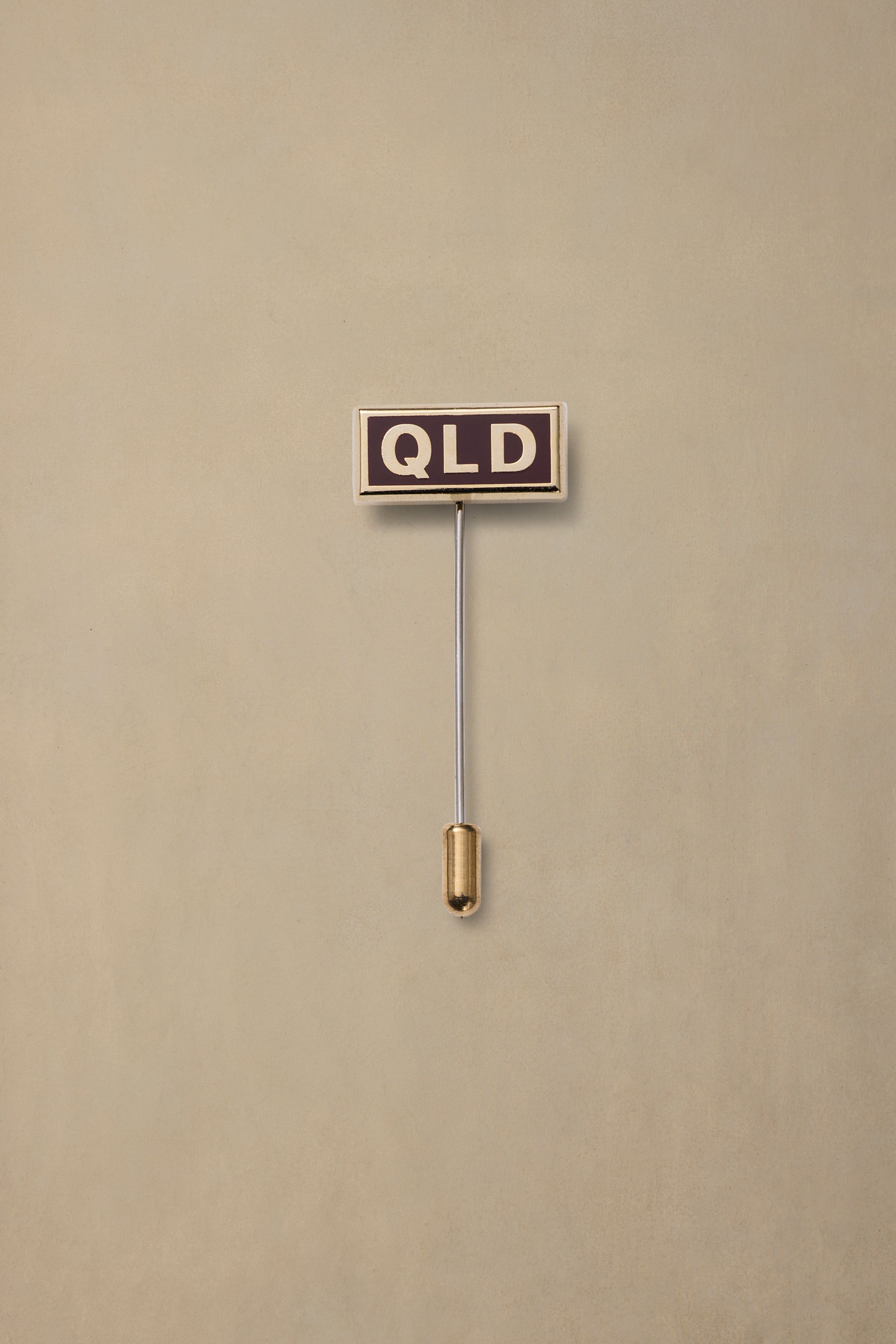 QLD state pin with dark enamel face and gold stem on neutral background