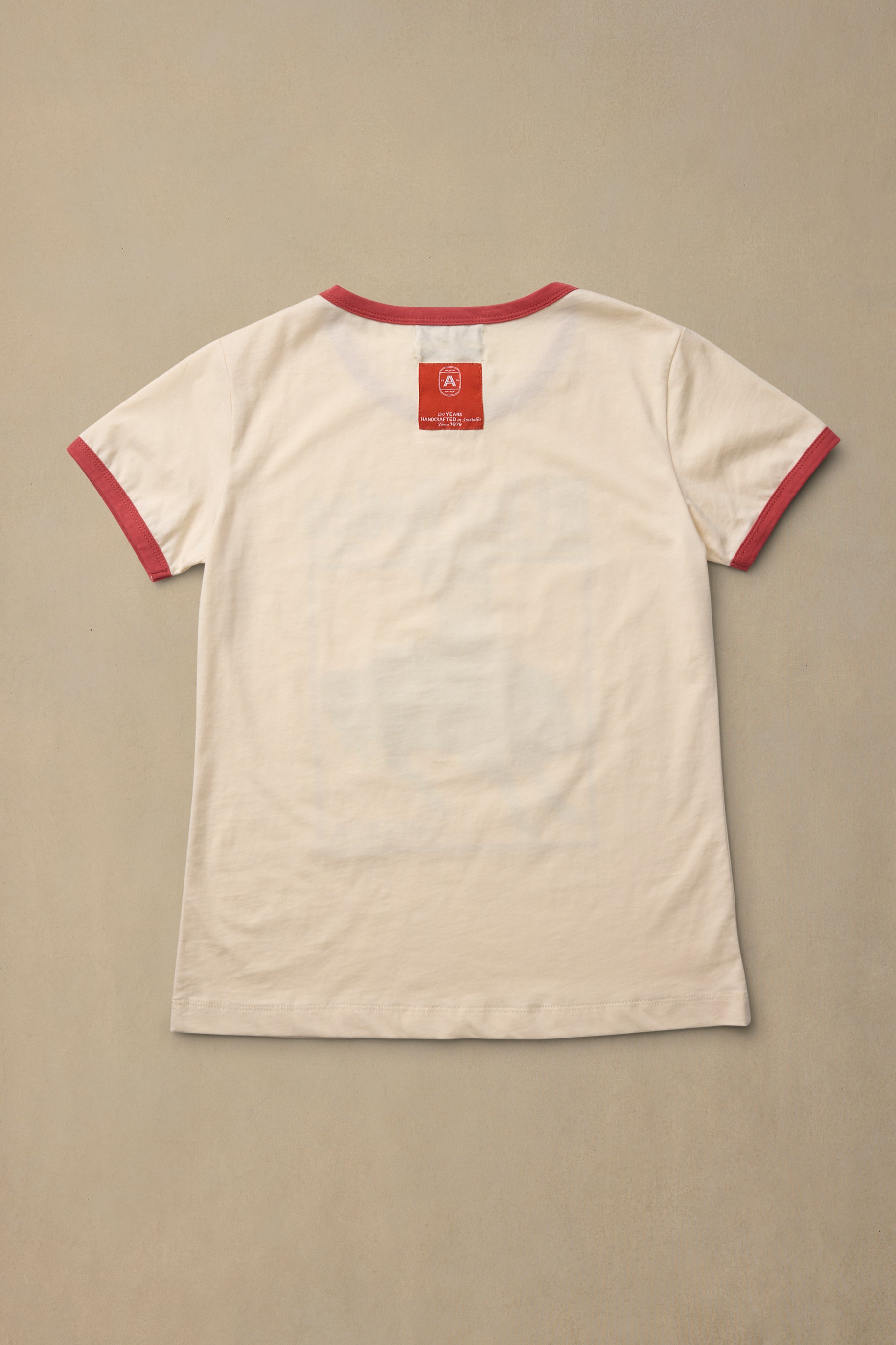 A white short-sleeve ringer T-shirt with red trim on the collar and sleeve cuffs, laid flat against a neutral beige background.