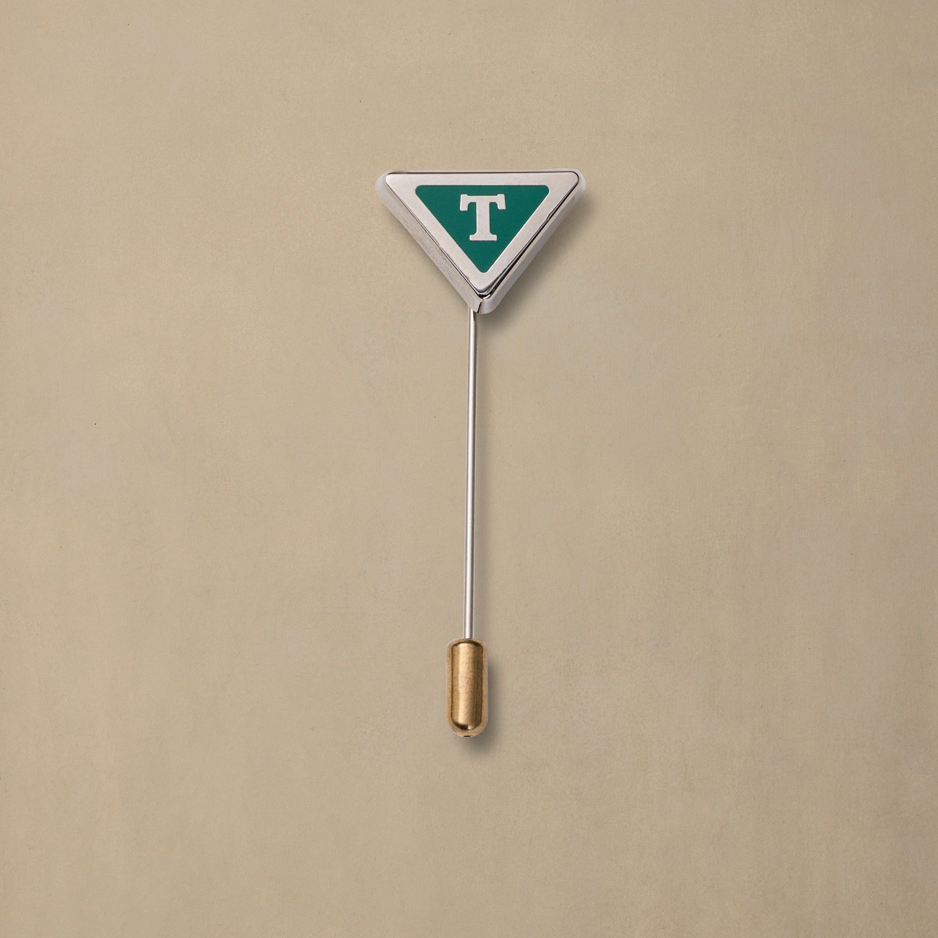 Triangular TAS State pin with teal and white enamel design, gold-plated stem, displayed on beige background