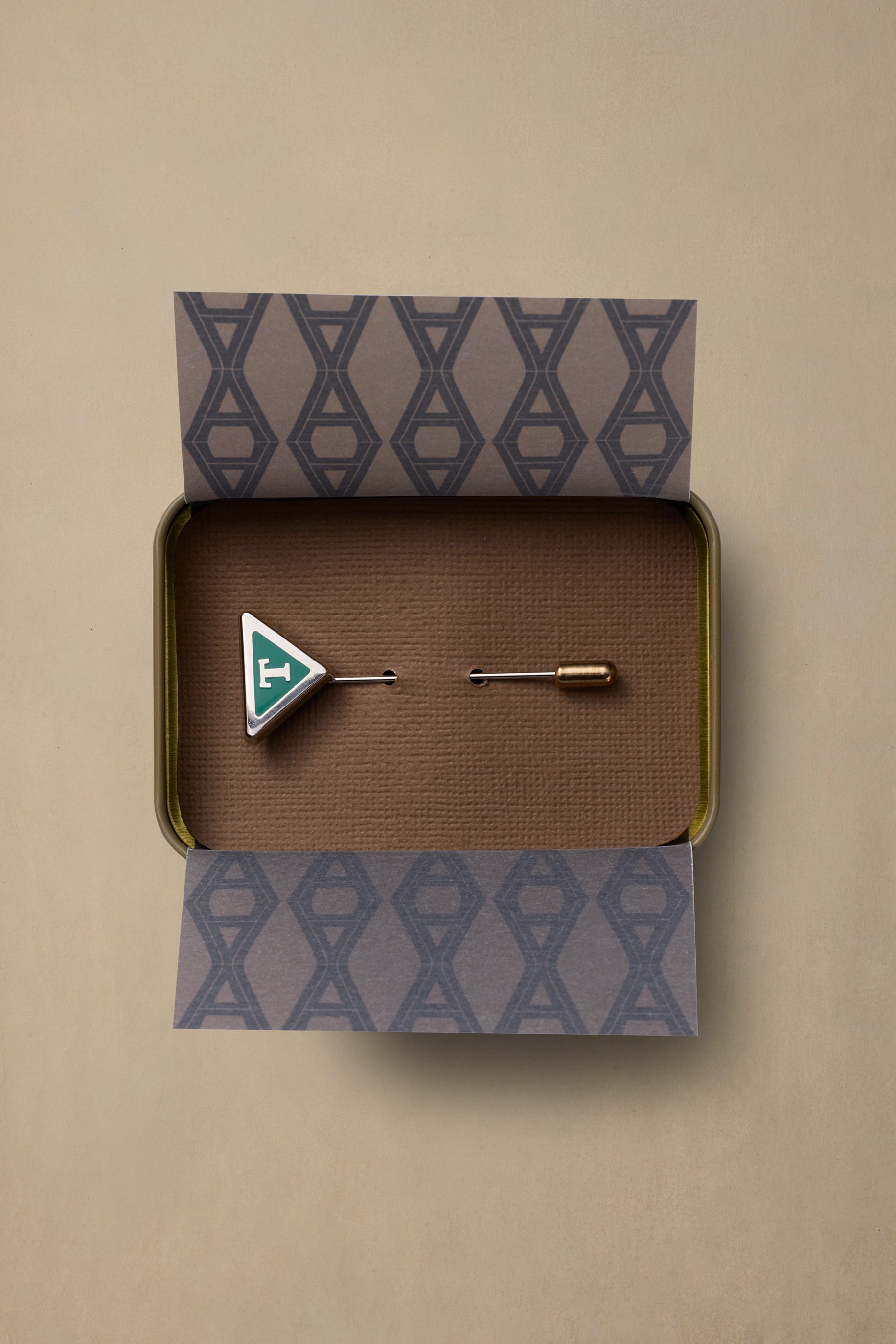 TAS State enamel pin with green triangle design in branded gift box with patterned tissue paper