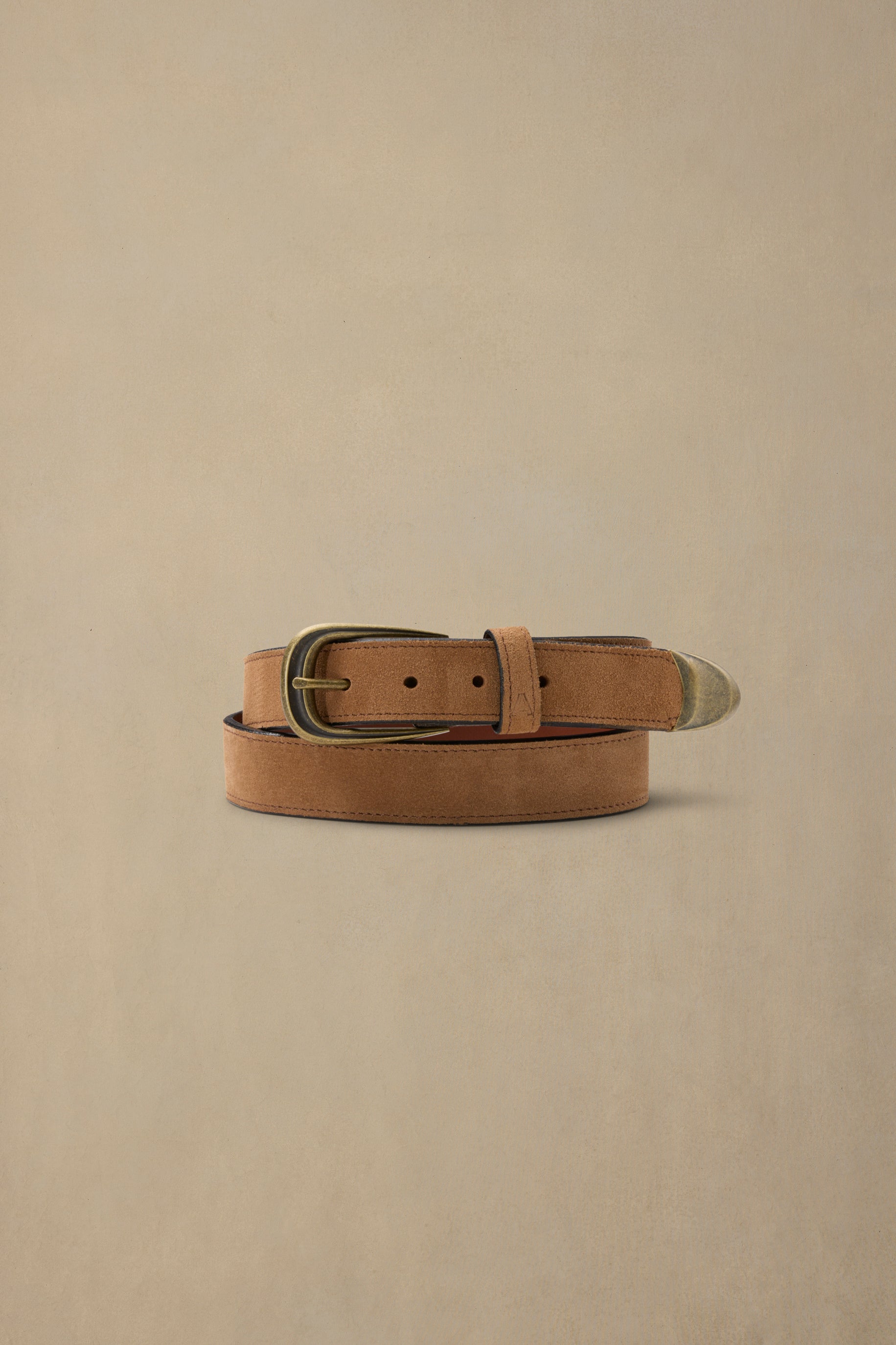 Tan suede belt with brass buckle and leather details coiled on neutral background