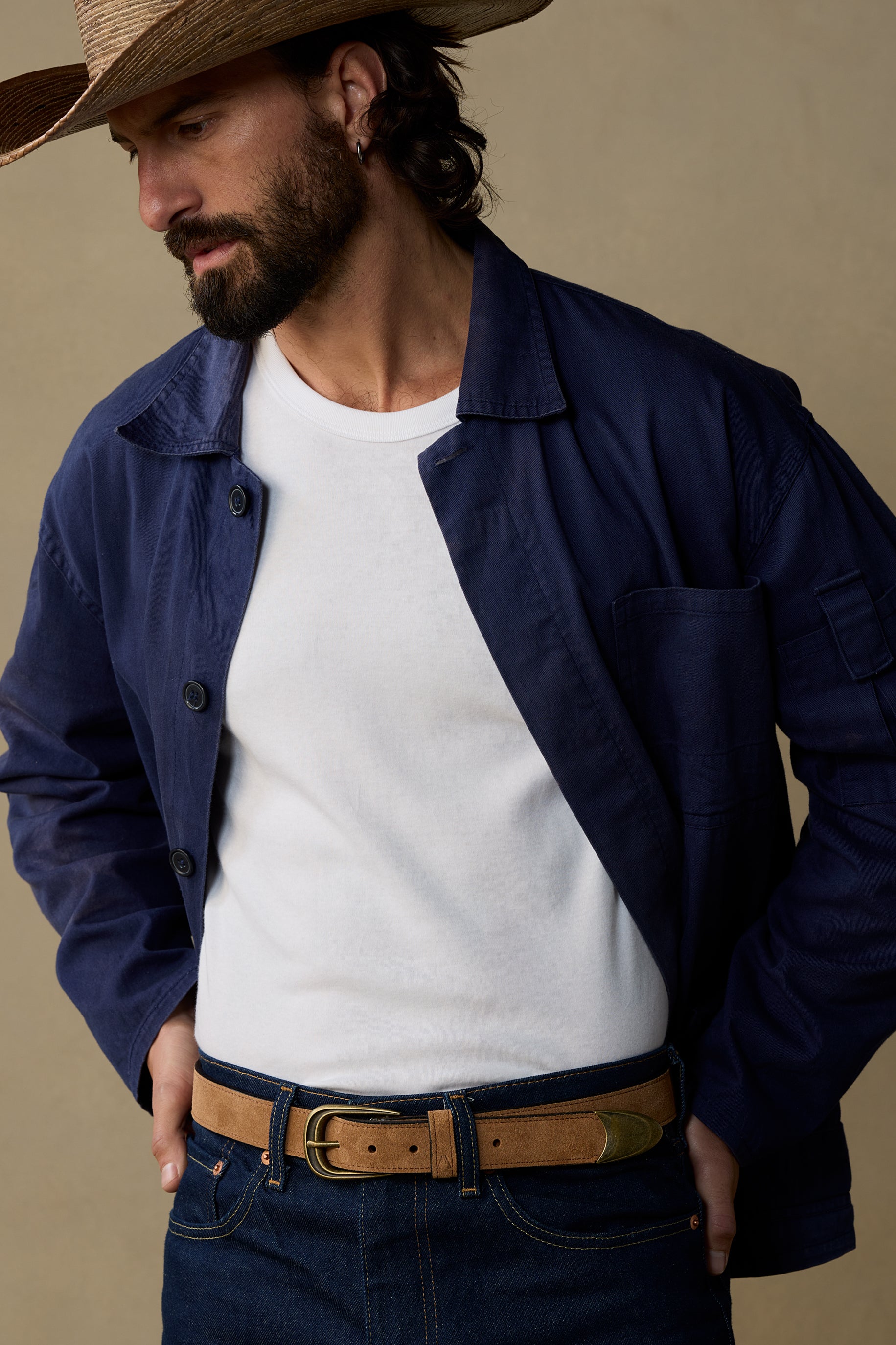 Tan suede belt with brass buckle worn with navy jacket and white t-shirt on neutral background