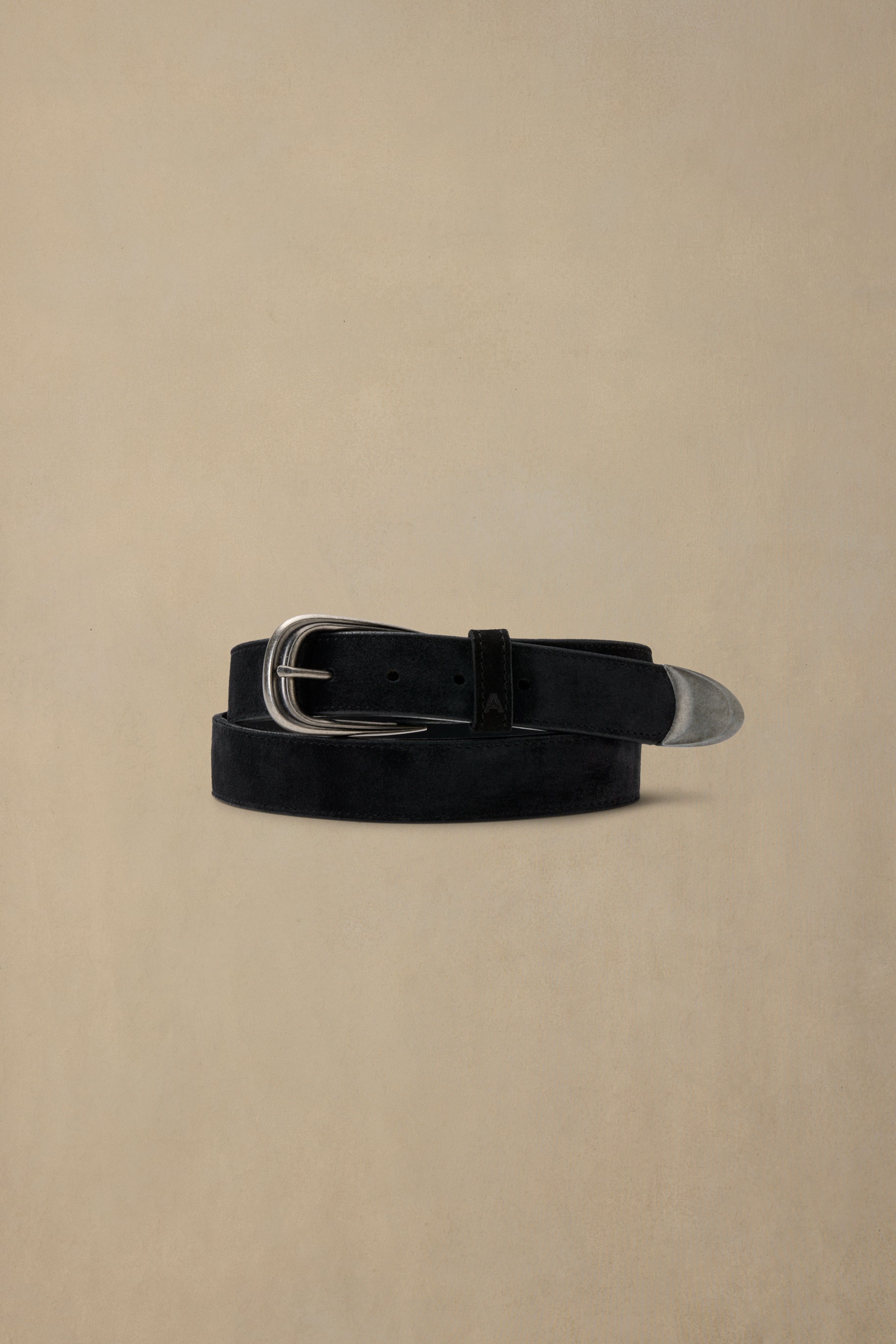 Black suede belt with silver buckle and metal tip on beige background