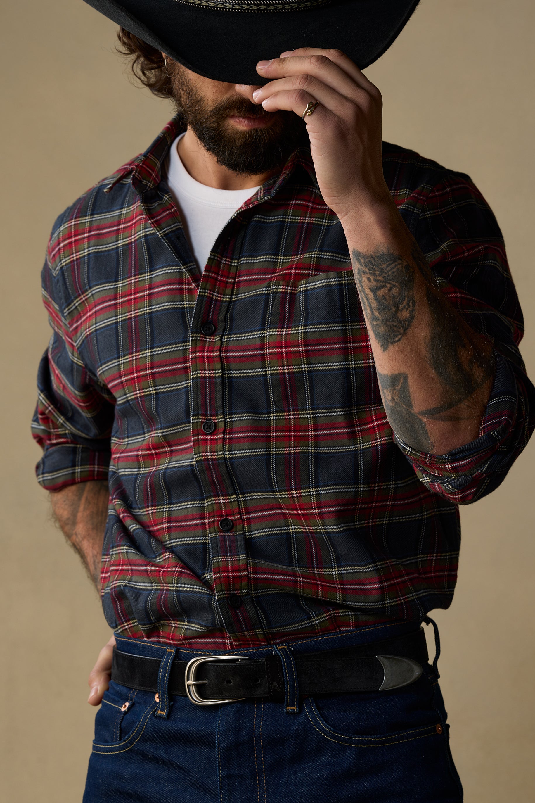 Black suede belt with pewter buckle worn with plaid shirt and jeans on beige background