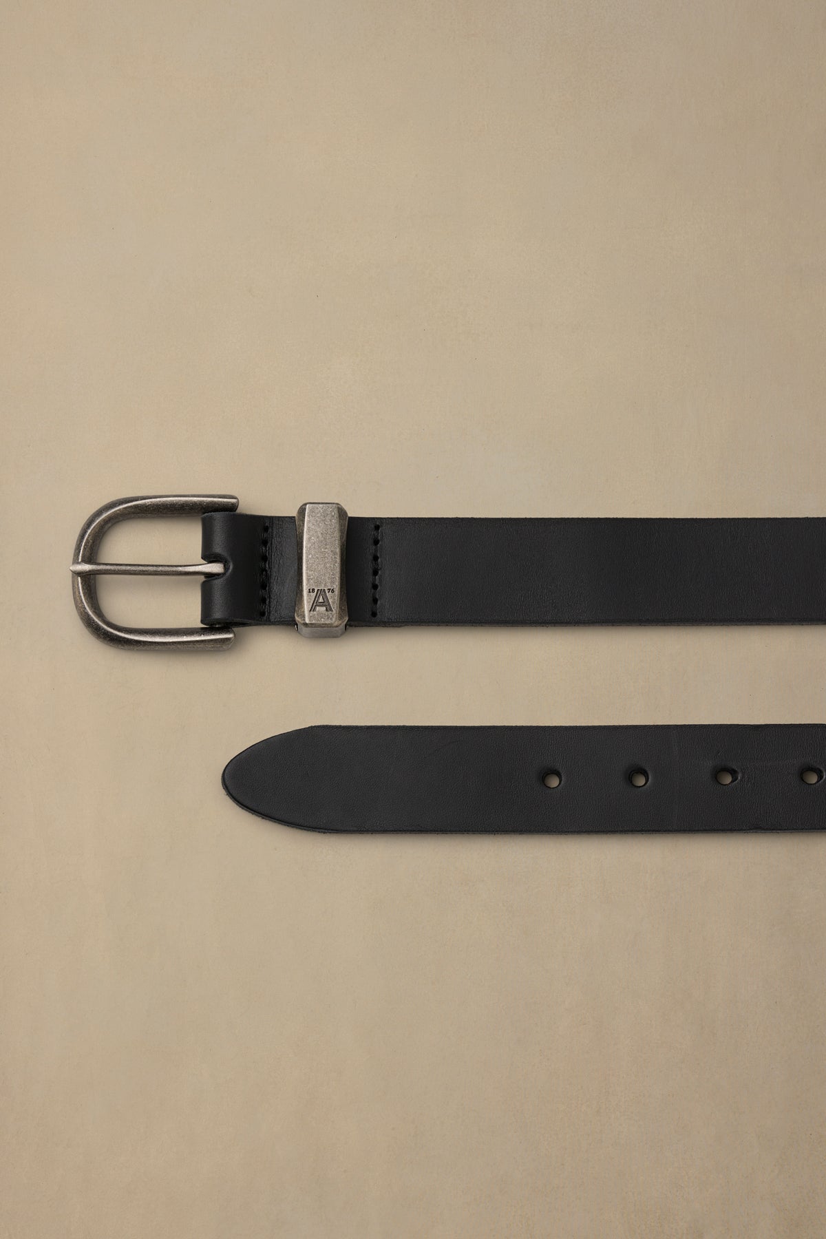 Black leather belt with pewter buckle and metal keeper detail, displayed flat on beige background