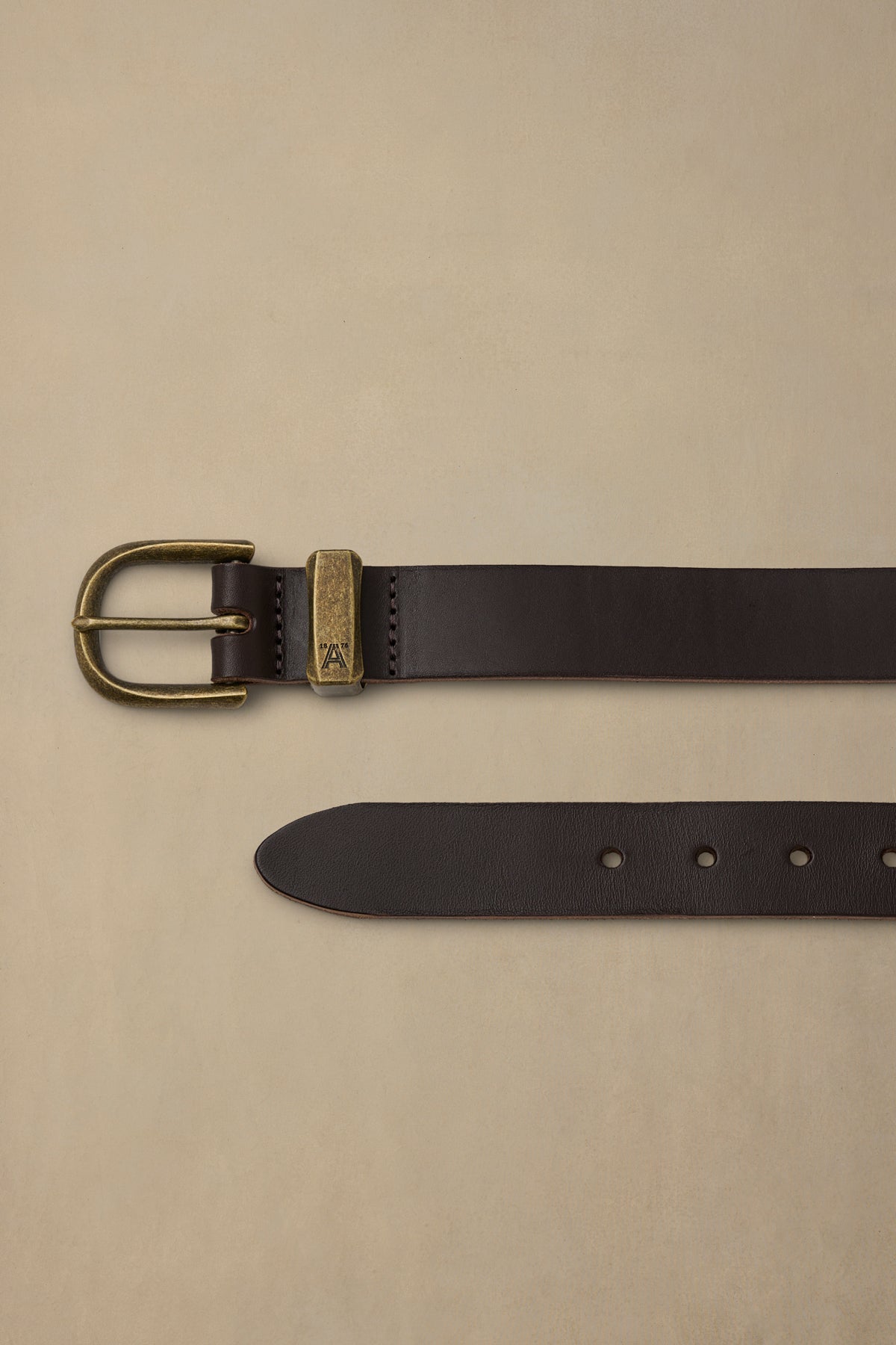 Dark brown leather belt with brass buckle and keeper, displayed flat on cream background showing front and folded sections