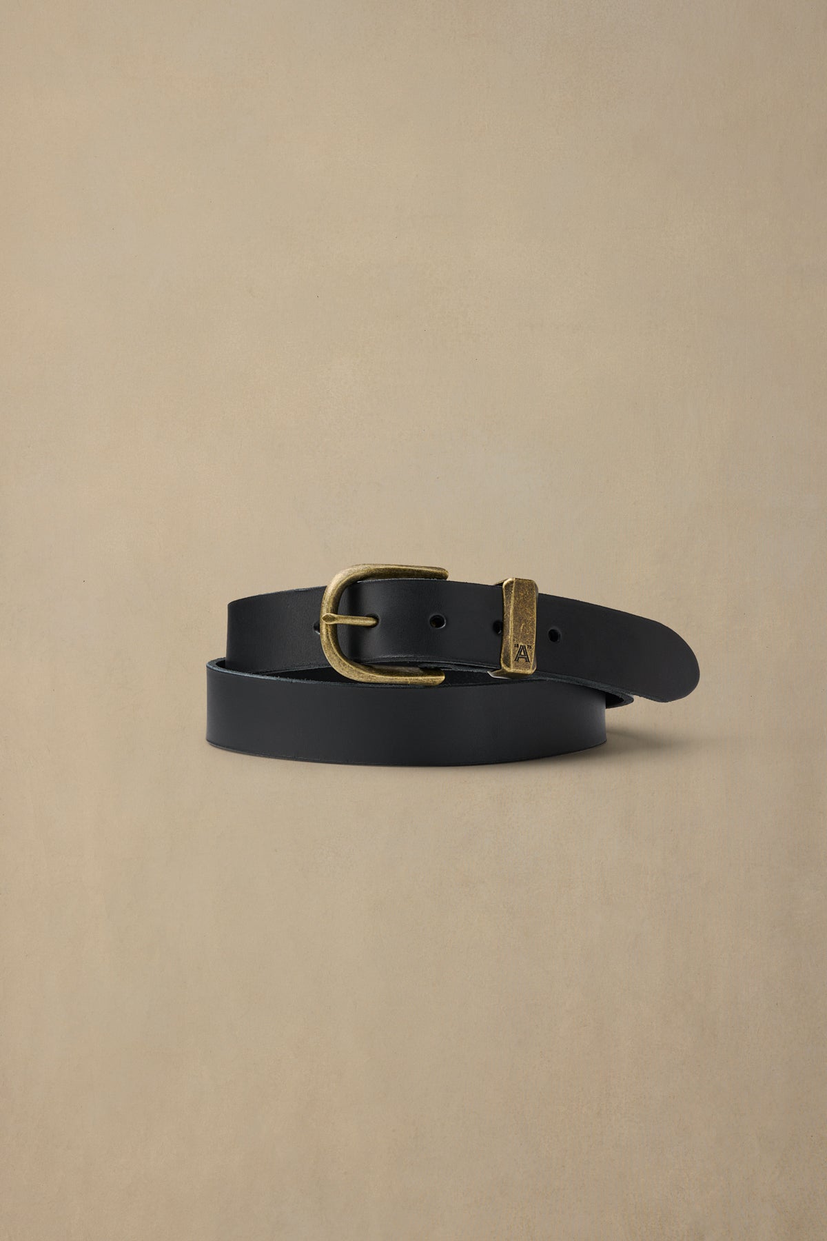 Black leather belt with brass buckle and keeper loop coiled on neutral background