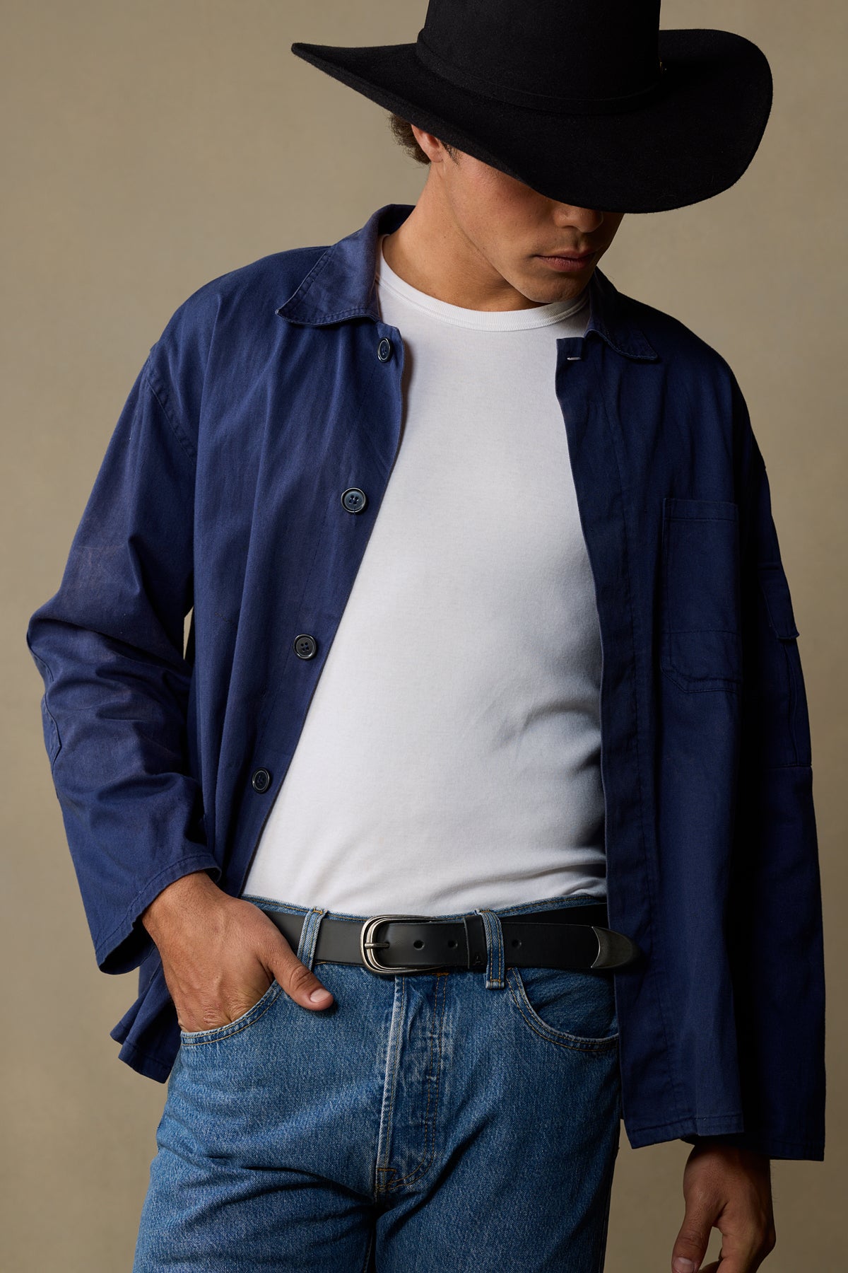 Black leather belt with silver buckle worn with navy shirt and white t-shirt on neutral background