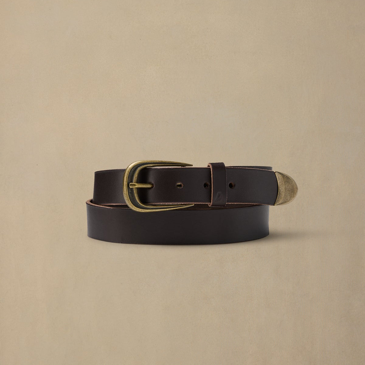 Dark brown leather belt with brass buckle and metal tip on beige background