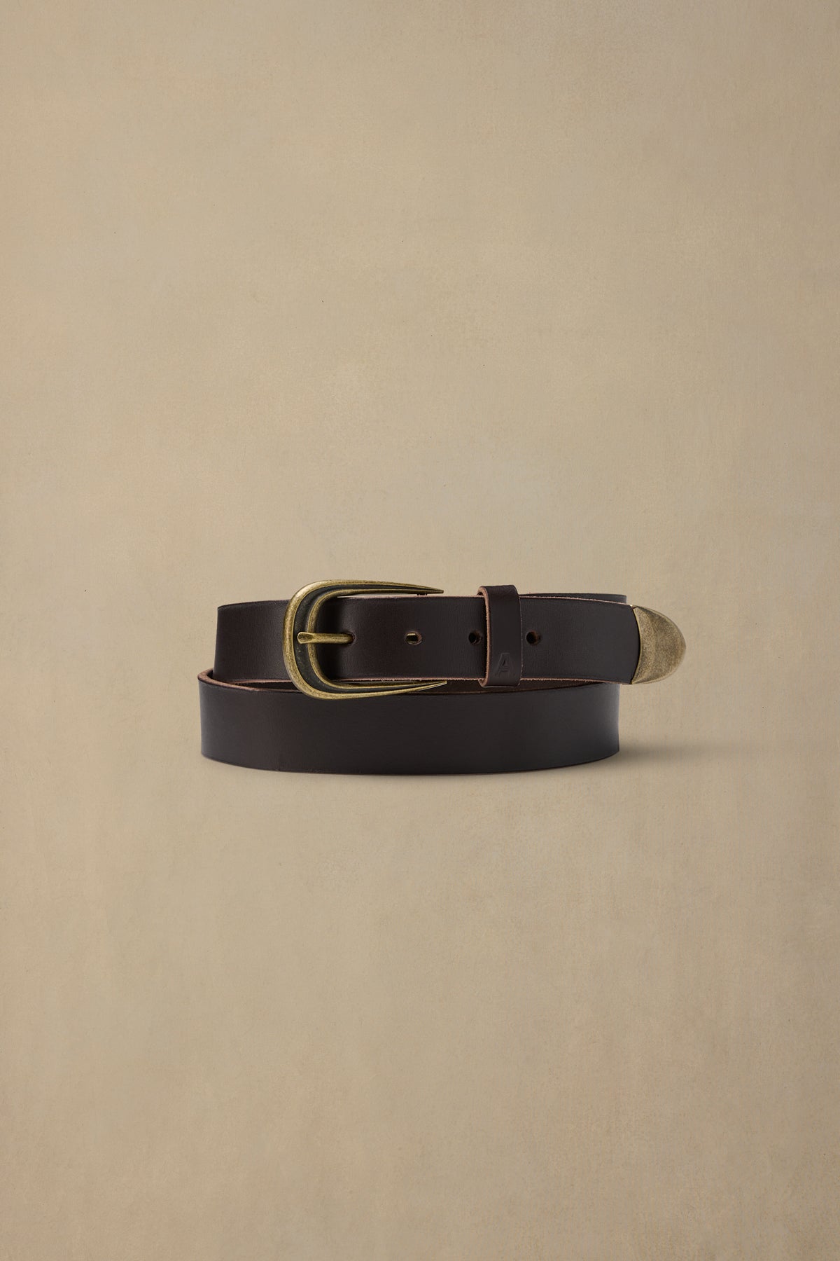 Dark brown leather belt with brass buckle and metal tip on cream background