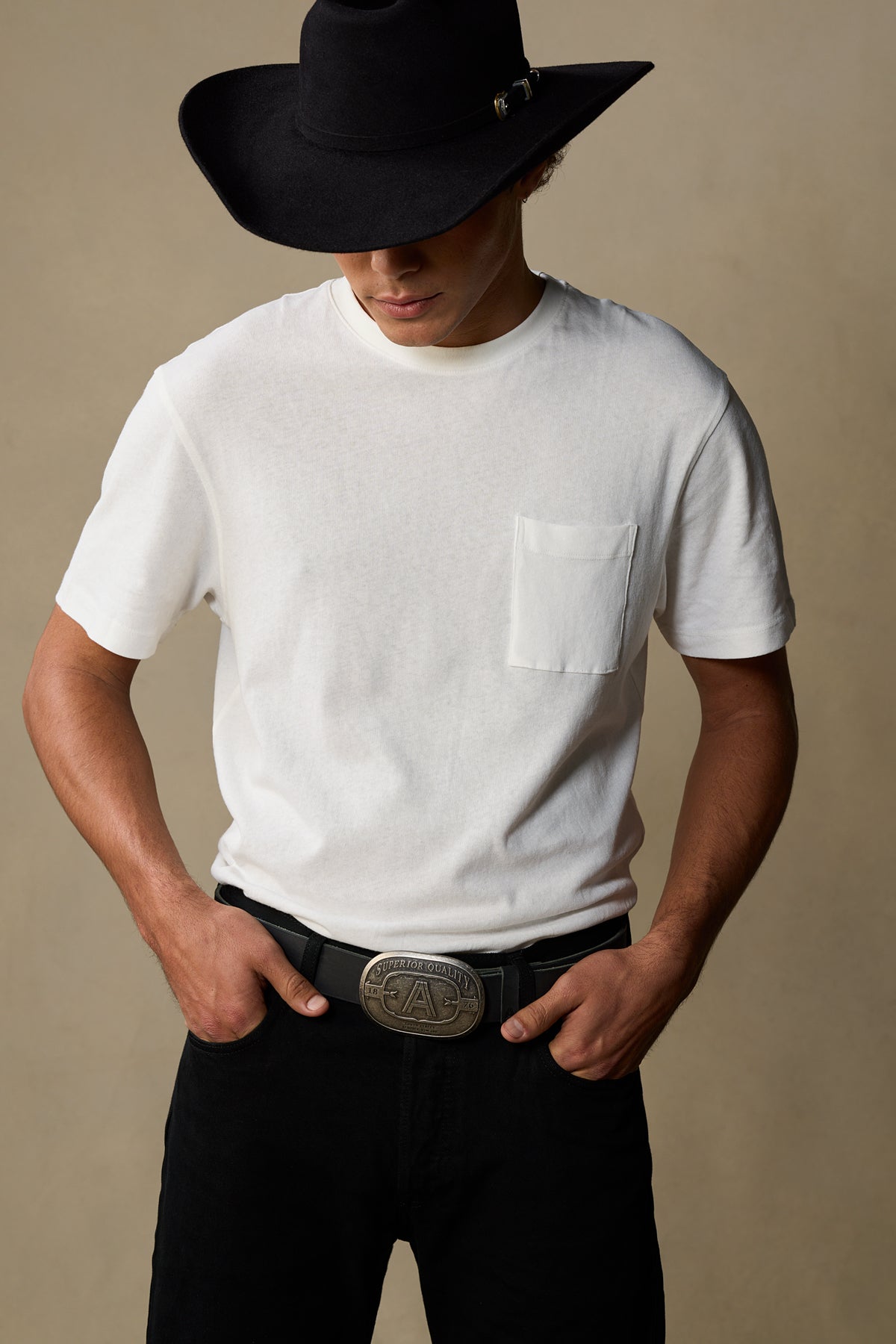 Black leather belt with metallic buckle worn with white pocket tee and black cowboy hat