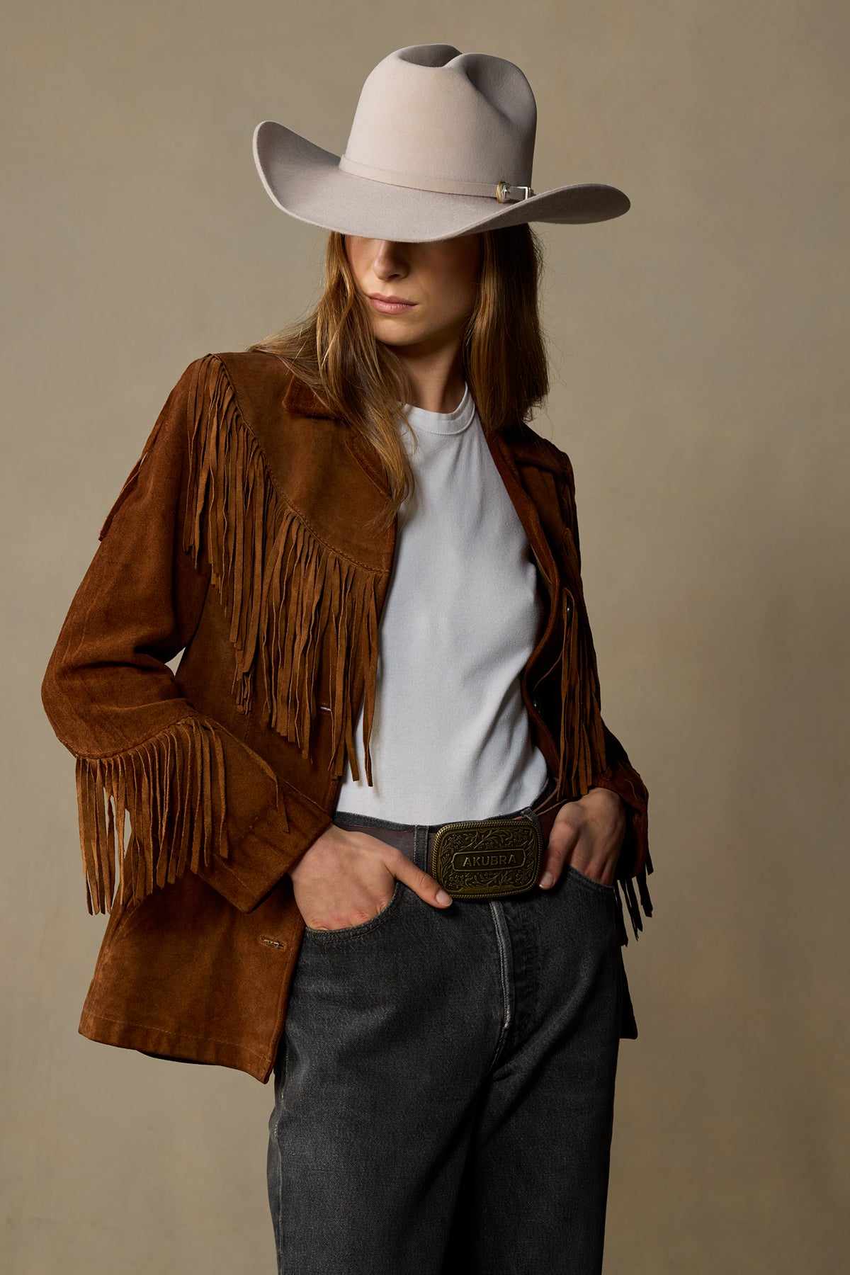 Brown leather fringe jacket belt with brass buckle worn by woman in cowboy hat