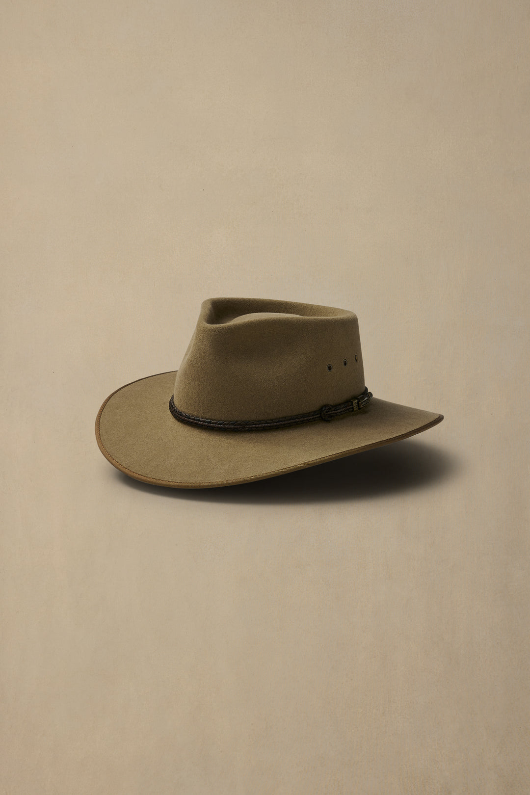 Brown felt cattleman hat with leather hatband and teardrop crown on neutral beige background