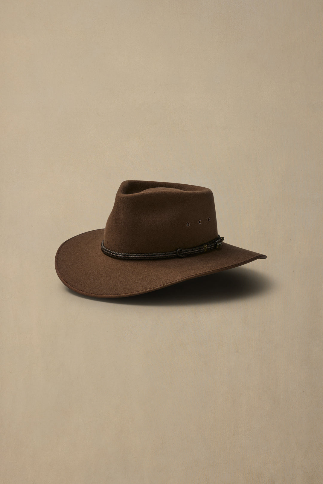 Brown felt cattleman hat with leather band and teardrop crown on neutral beige background