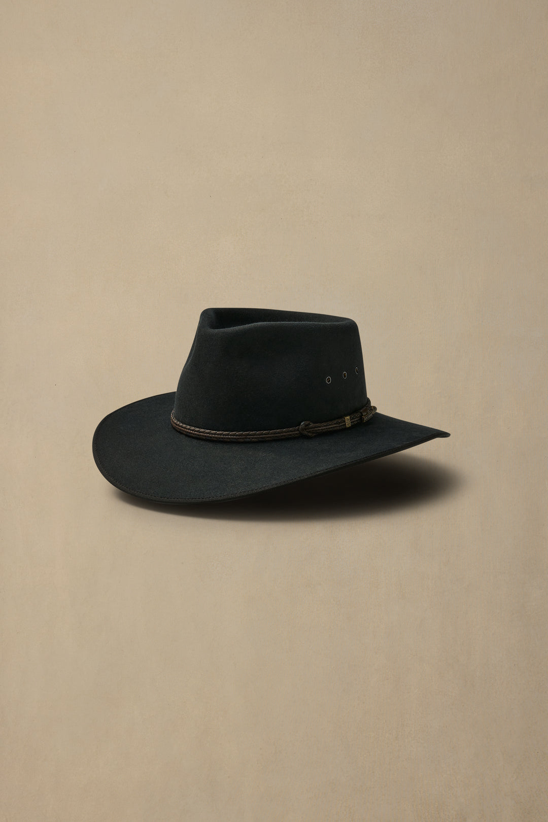 Dark grey felt cowboy hat with leather hatband photographed at angle on neutral beige background