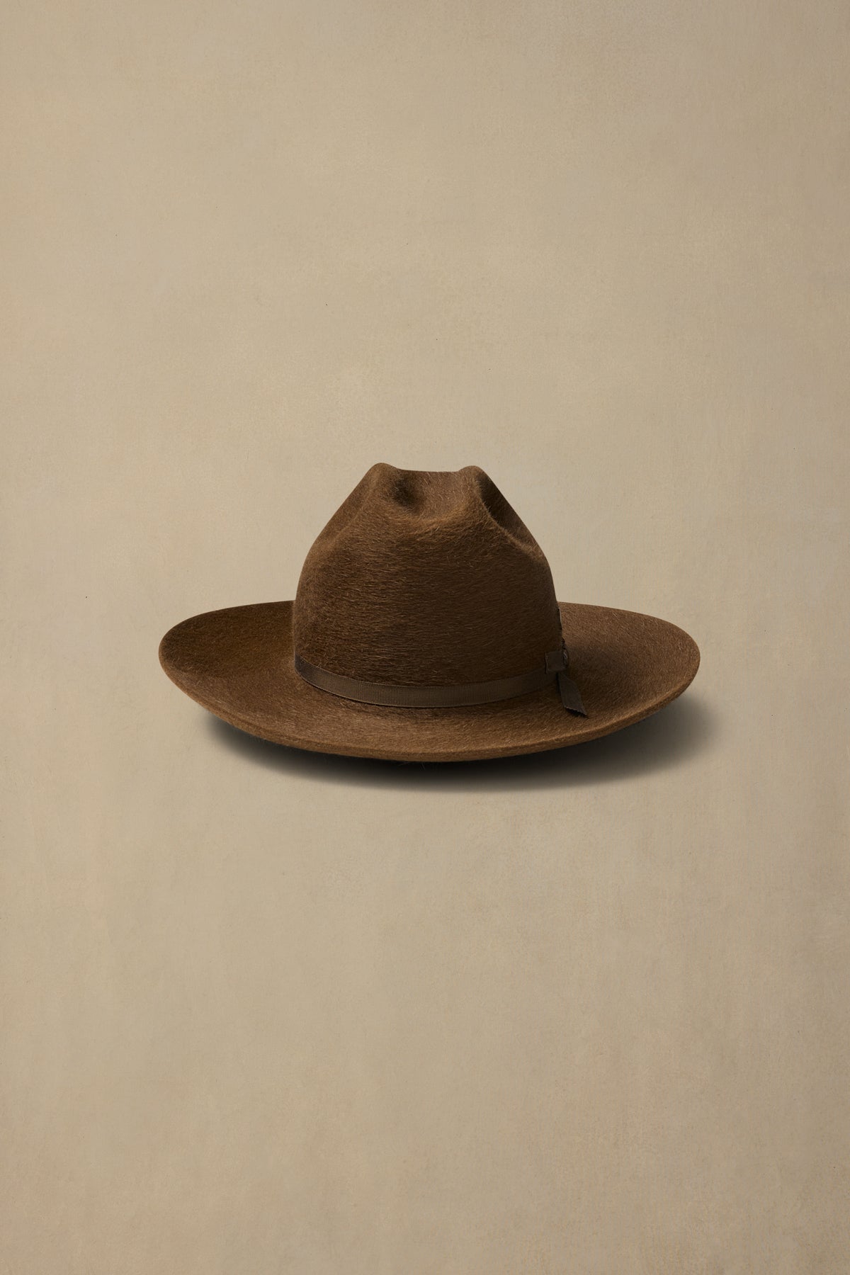 Brown rabbit fur felt cowboy hat with leather band on neutral background