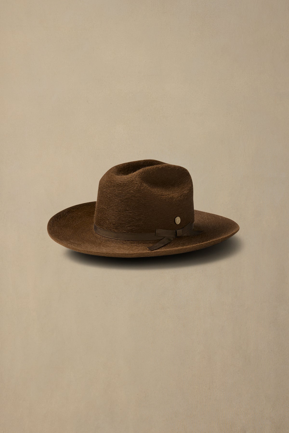 Brown rabbit fur felt cowboy hat with leather band on cream background