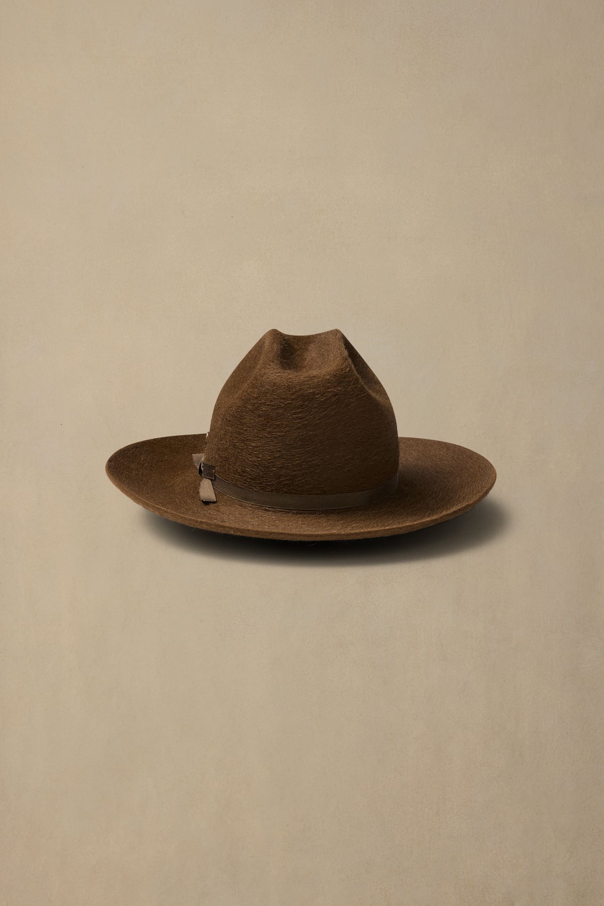 Brown rabbit fur felt cowboy hat with leather band on neutral beige background