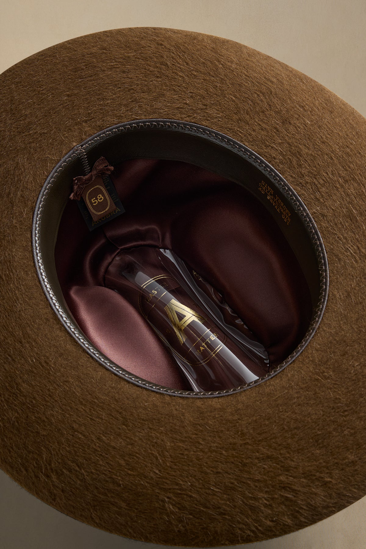 Tan rabbit fur felt hat displayed open, showing burgundy interior lining and vintage fragrance bottle inside