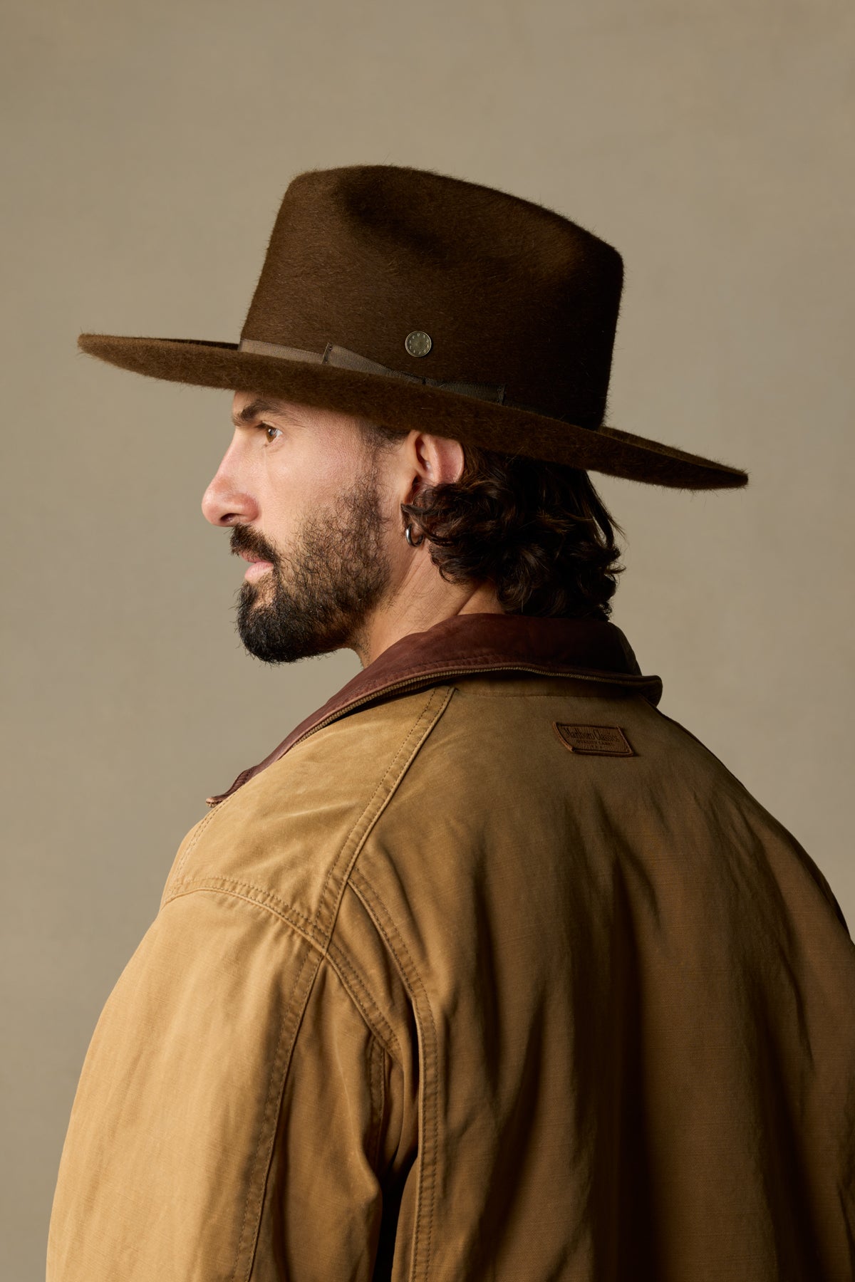 Brown fur felt cowboy hat with silver band detail on man wearing tan jacket, side profile view