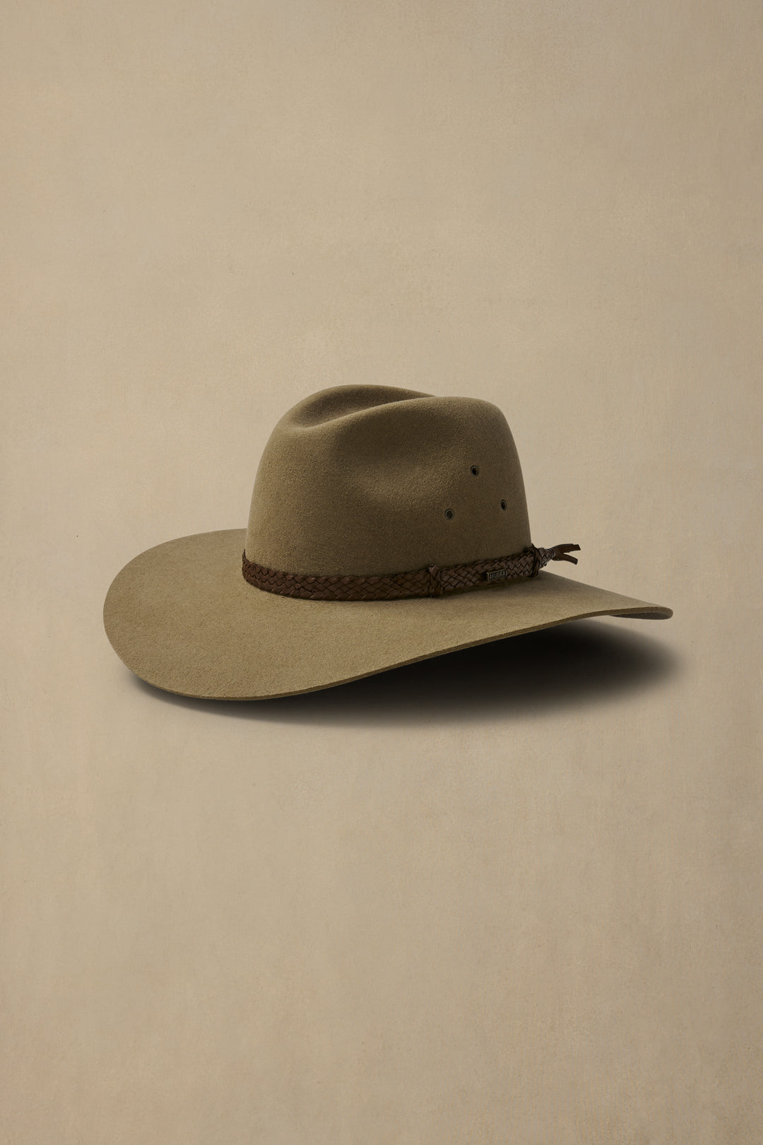 Brown felt cowboy hat with wide brim and braided leather hatband, displayed on neutral beige background