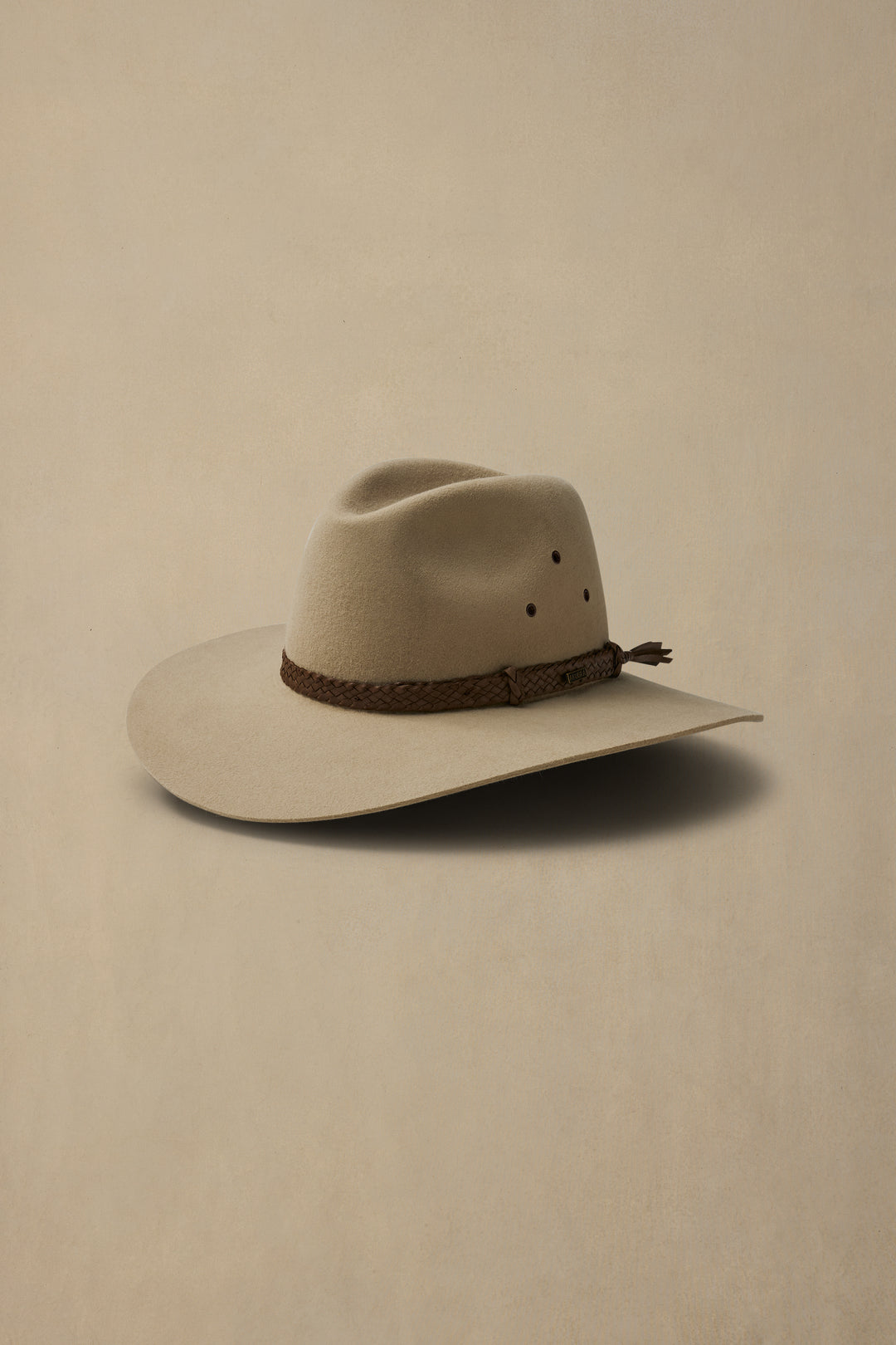 Sand-colored felt hat with wide brim and braided leather band, photographed against neutral beige background