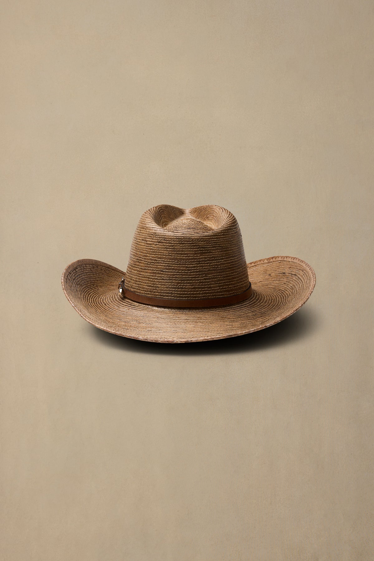 Tan woven straw cowboy hat with brown leather band against neutral beige background