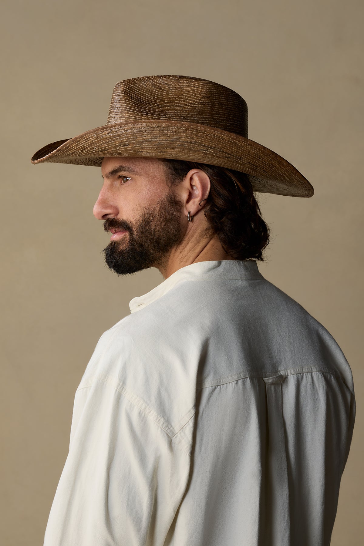 Man wearing tan woven straw cowboy hat with white shirt, shown in profile against neutral beige background