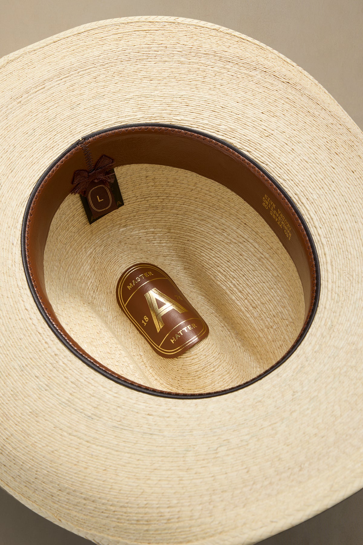 Close-up top-down view of a straw cowboy hat showing the interior crown, brown leather band, and a branded paper tag inside.