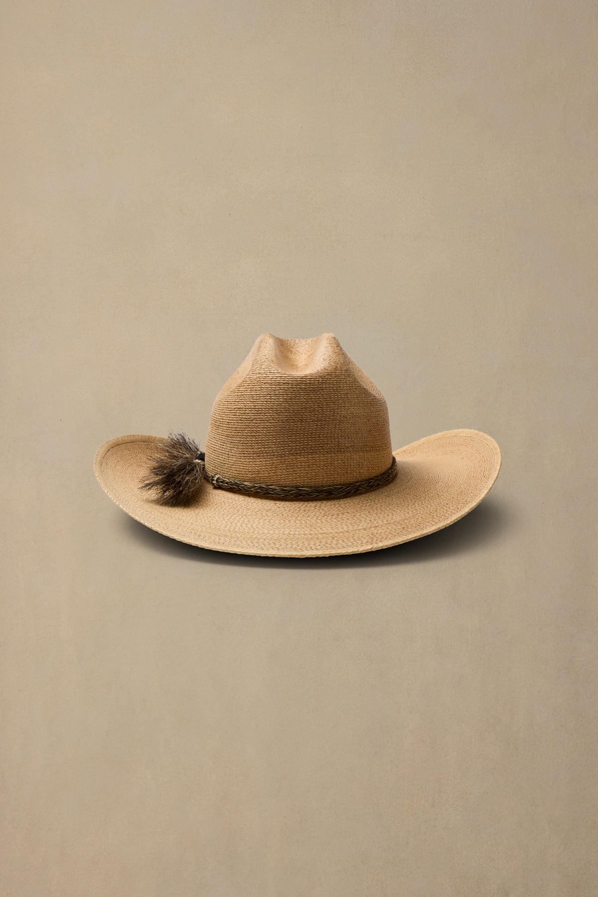 A dark tan woven cowboy hat with a dark brown band and a matching tassel accent, displayed against a solid beige background.
