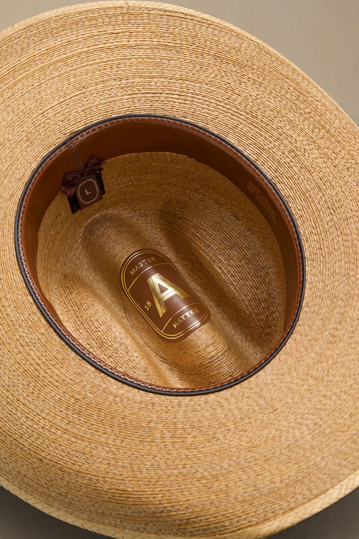 Close-up top-down view of a woven straw cowboy hat showing the tan interior, dark brown band, and a gold-toned brand plaque on the inside crown.