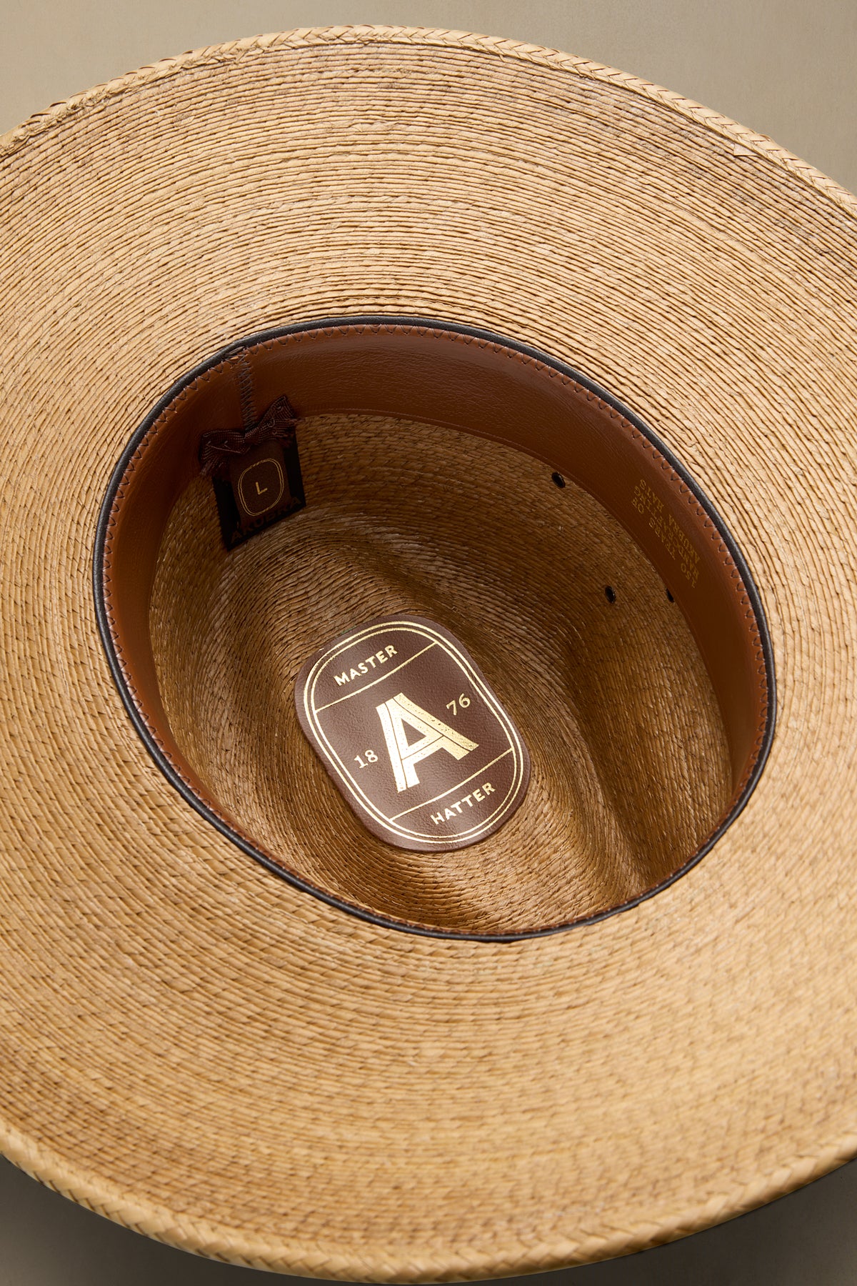 Close-up top-down view of a woven straw cowboy hat showing the tan interior, dark brown band, and a gold-toned brand plaque on the inside crown.