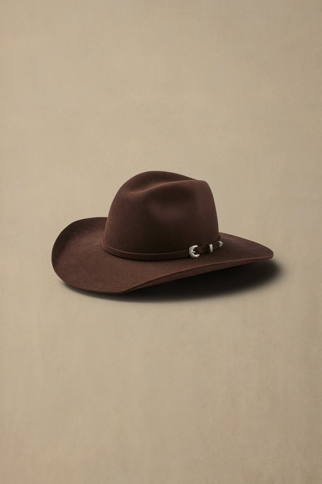 Brown fur felt cowboy hat with silver band detail on neutral beige background