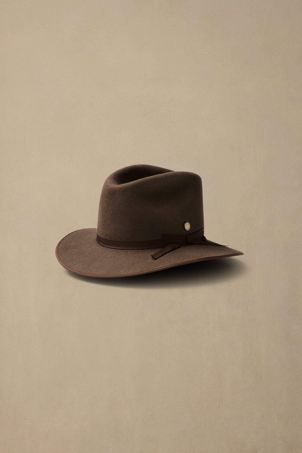 Brown felt cowboy hat with dark band and metal accent on neutral background