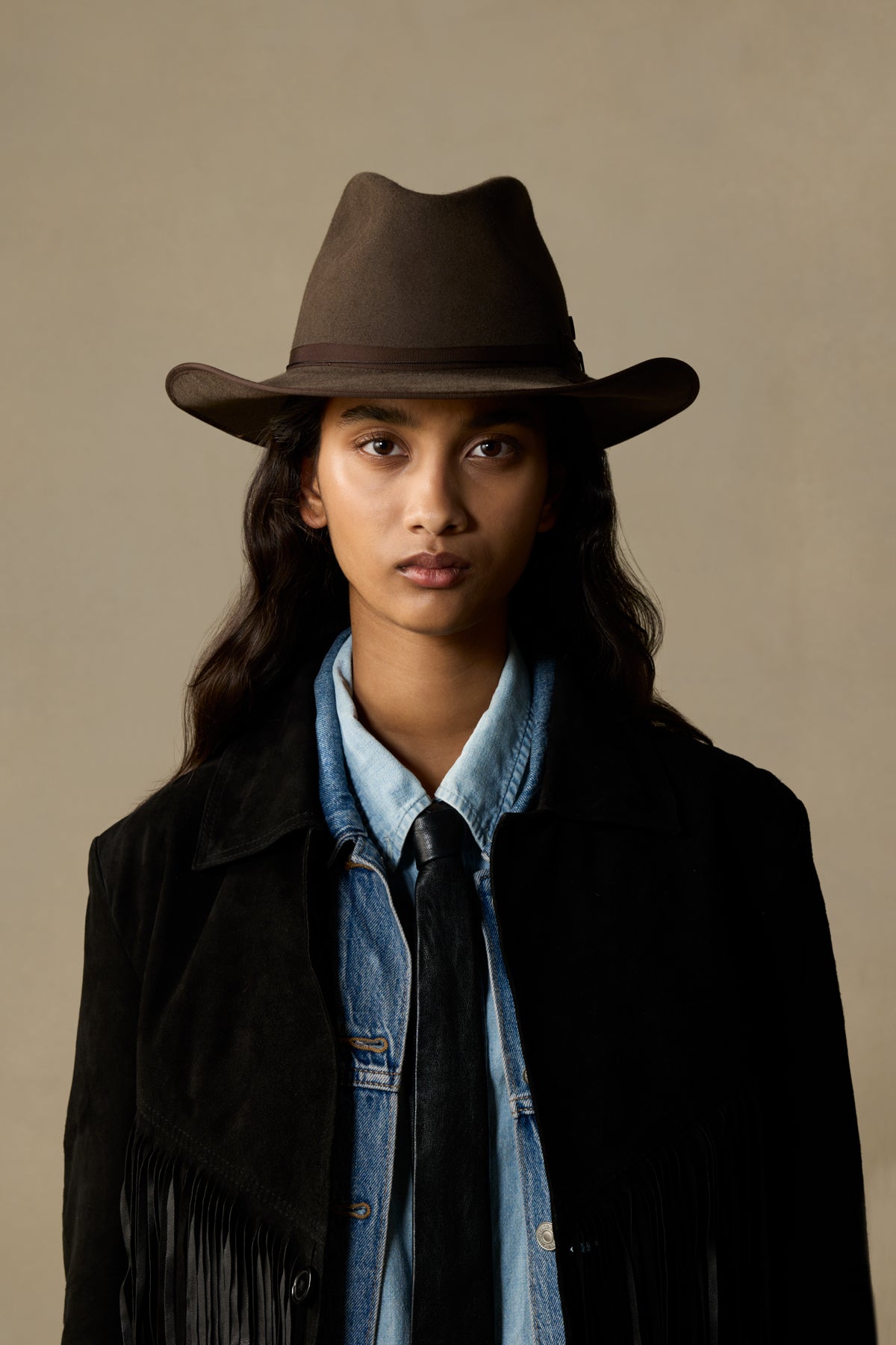 Mid brown fur felt cowboy hat with wide brim on model wearing denim shirt and black fringe jacket