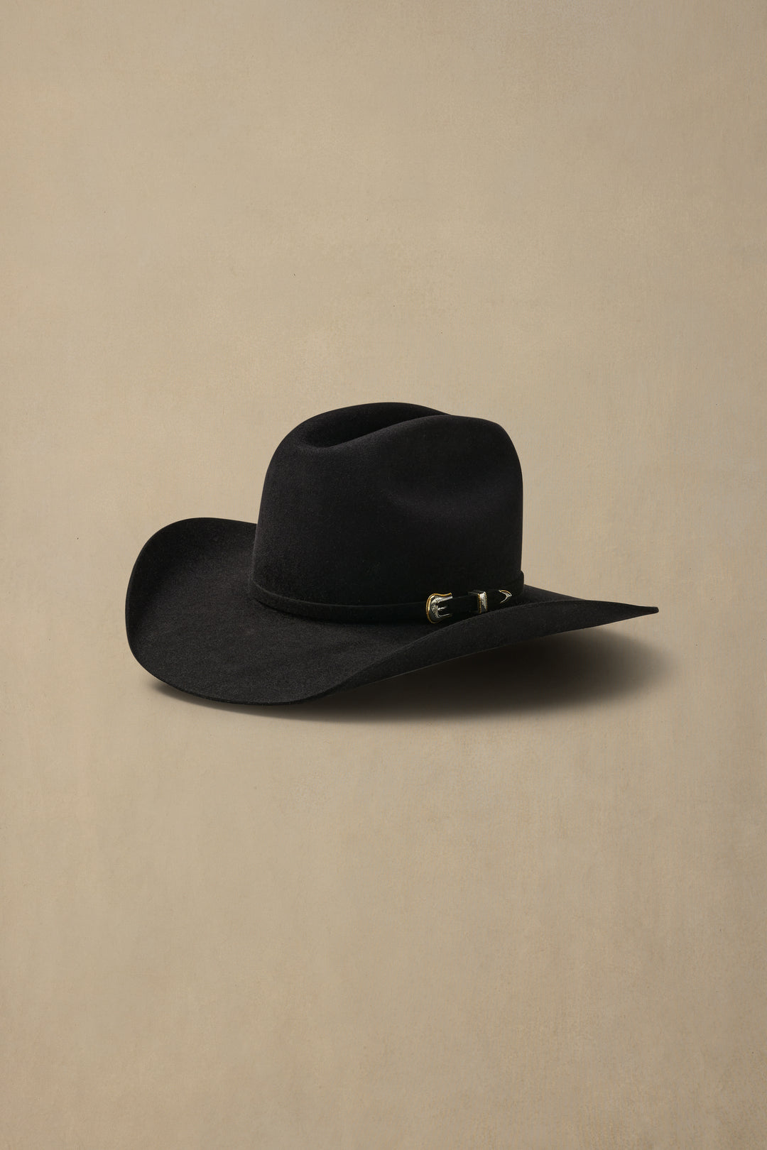 Black felt cowboy hat with cattleman crown and decorative metal band detail on neutral beige background